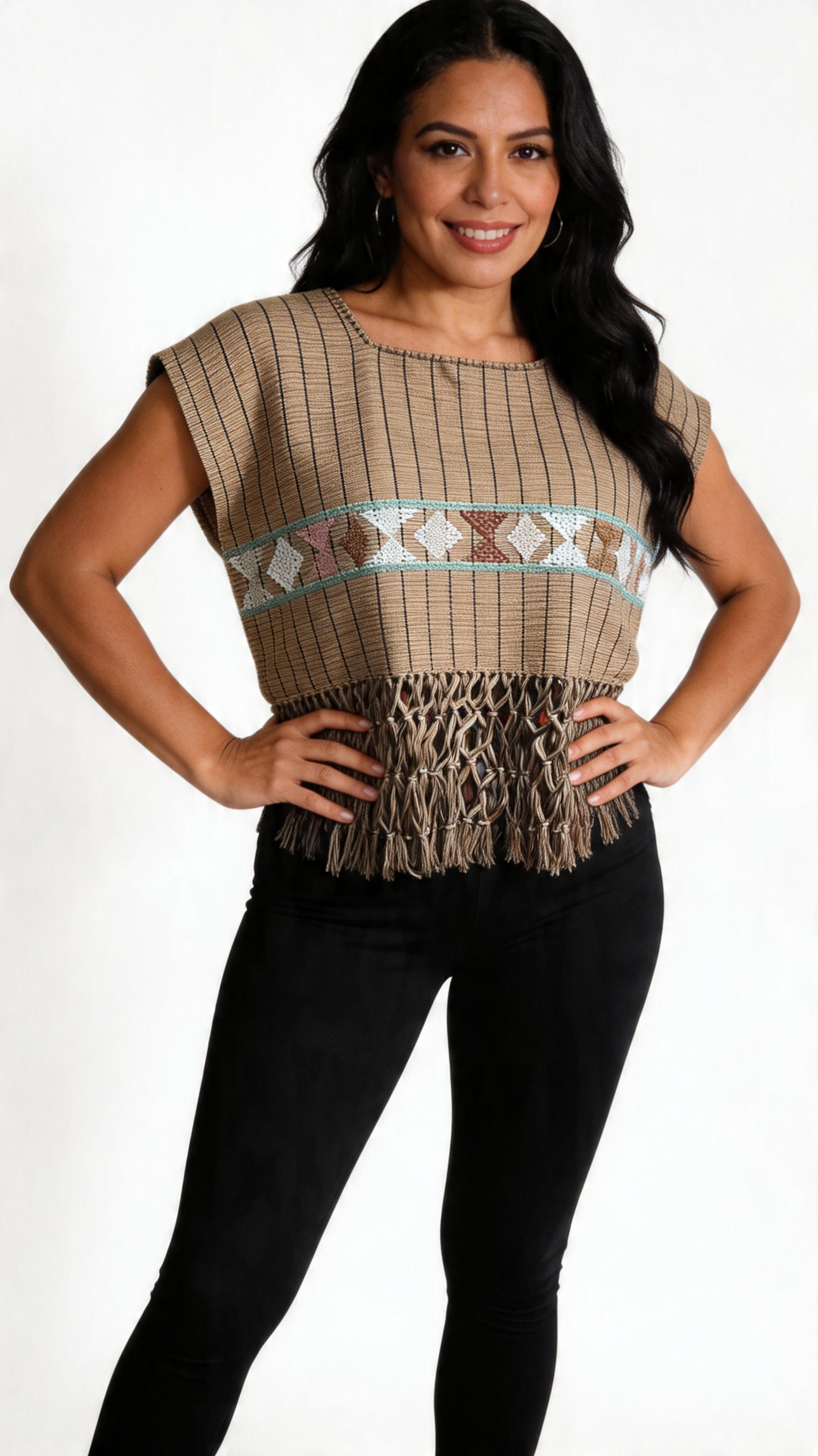 Woman with long black hair smiling, wearing a brown fringed top with geometric patterns and black pants, standing with hands on hips against a white background.