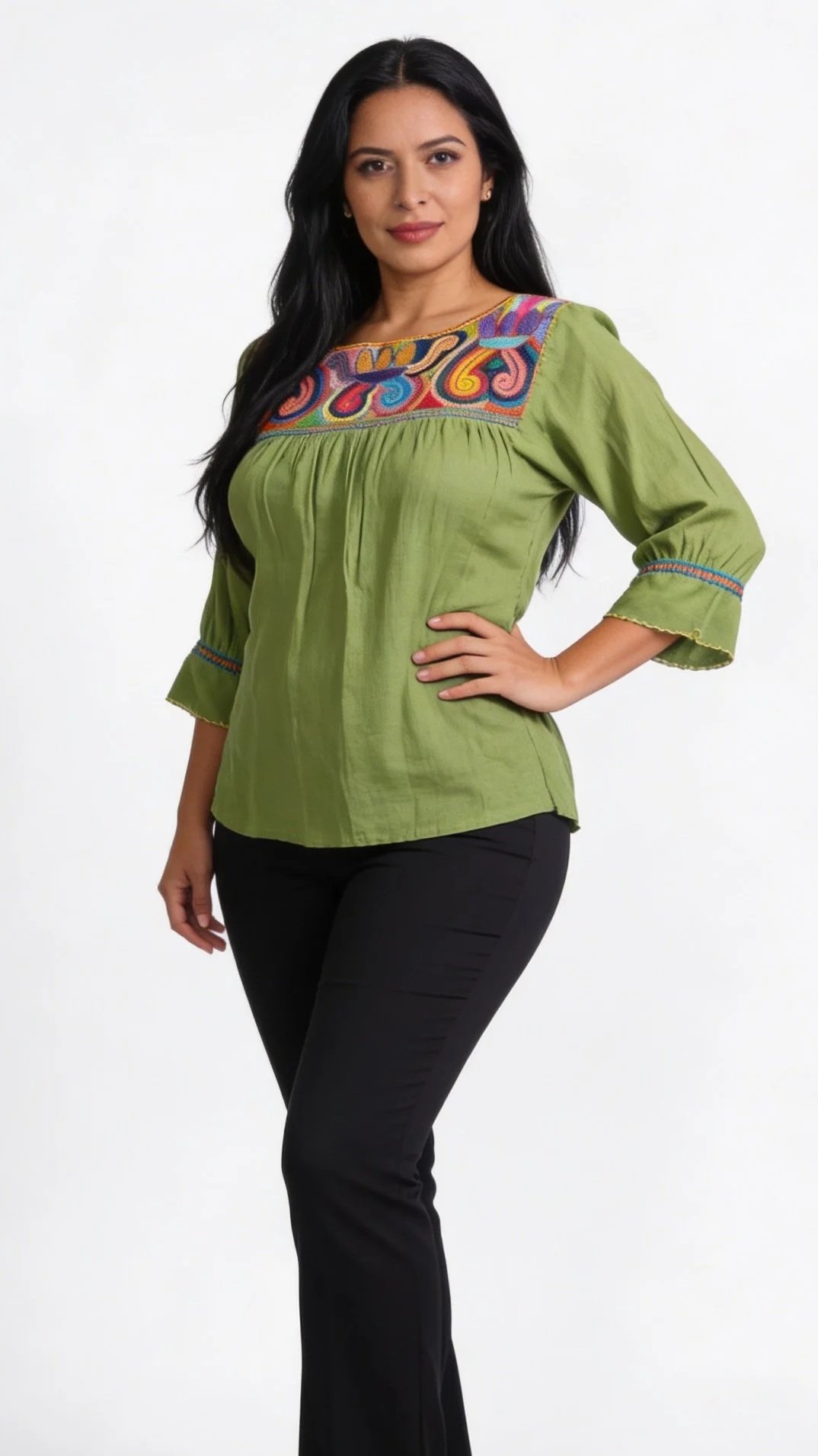 Woman with long black hair wearing a green embroidered blouse and black pants against a plain white background.