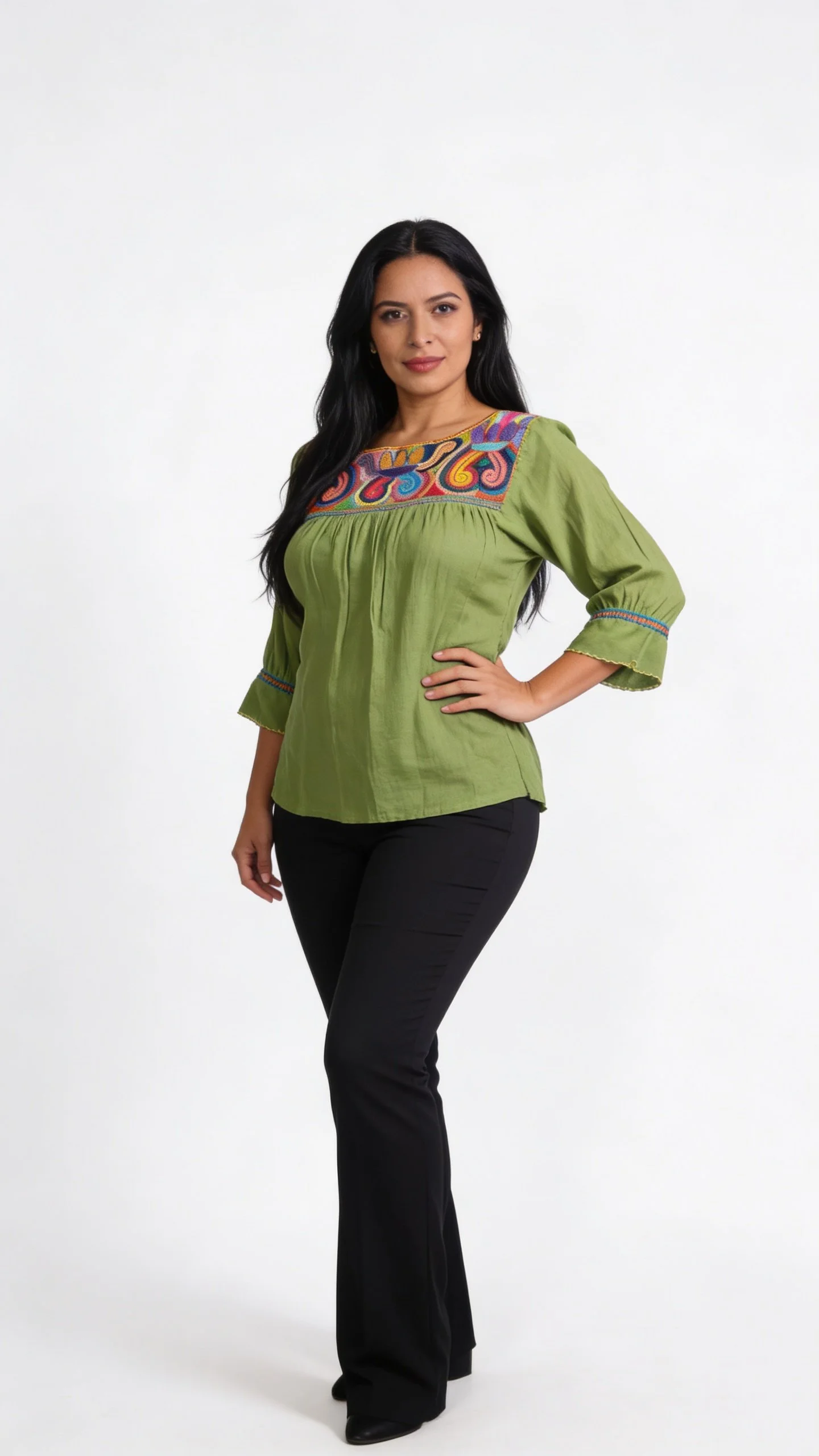 Woman with long black hair wearing a green embroidered top and black pants against a white background.
