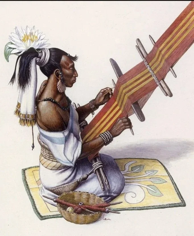 An indigenous person wearing traditional clothing, jewelry, and a feathered headdress, sitting on a decorated mat, holding a long wooden ceremonial spear or staff with carvings, and a basket containing traditional tools or objects beside them.