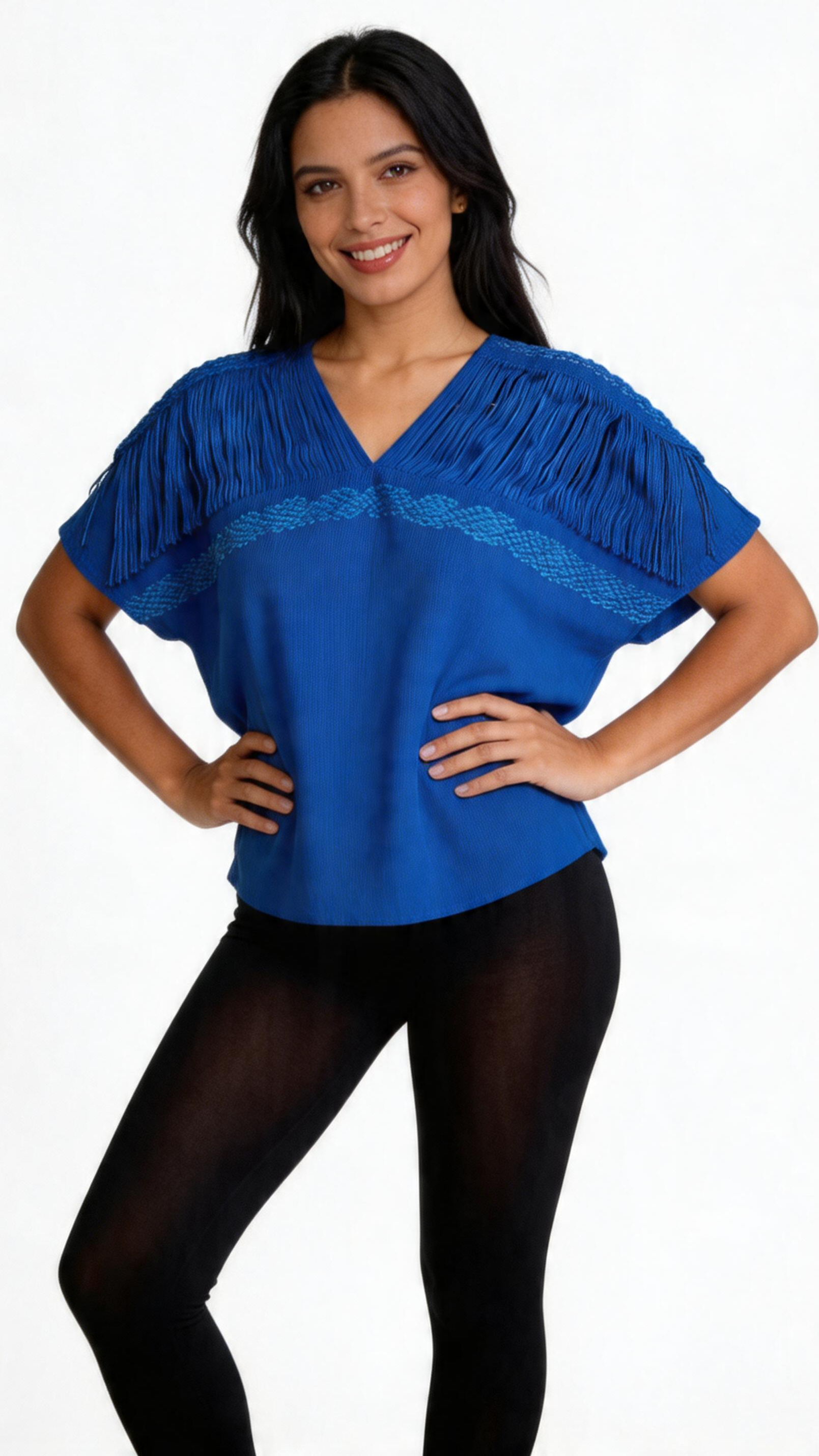 A woman with dark hair wearing a blue top with fringe details and black tights, standing with hands on hips against a white background.