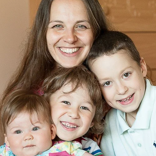 A woman smiling with three children, all of whom are smiling in a group portrait.