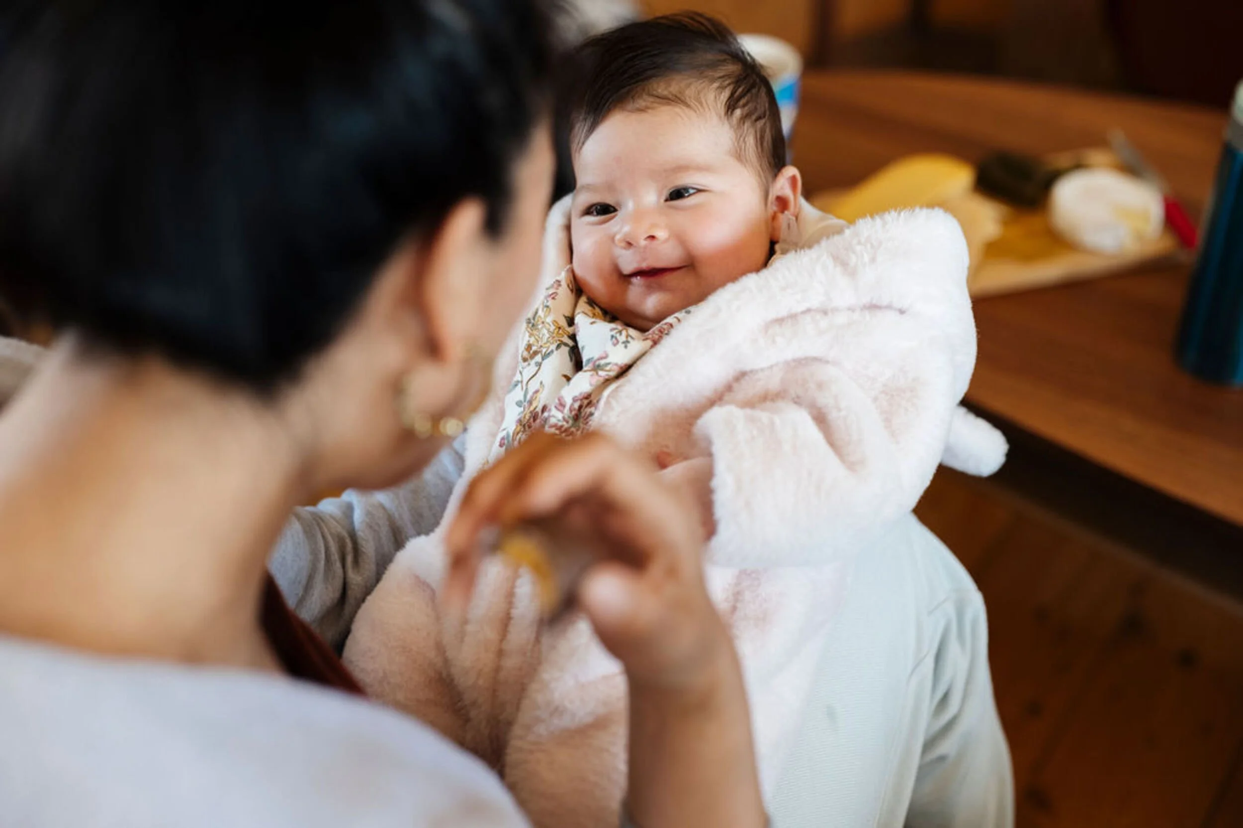 A smiling baby being held by a mother with dark hair.