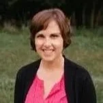 A woman with short brown hair smiling outdoors, wearing a pink top and black cardigan.