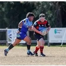 Two young rugby players competing for the ball during a game on a grassy field.