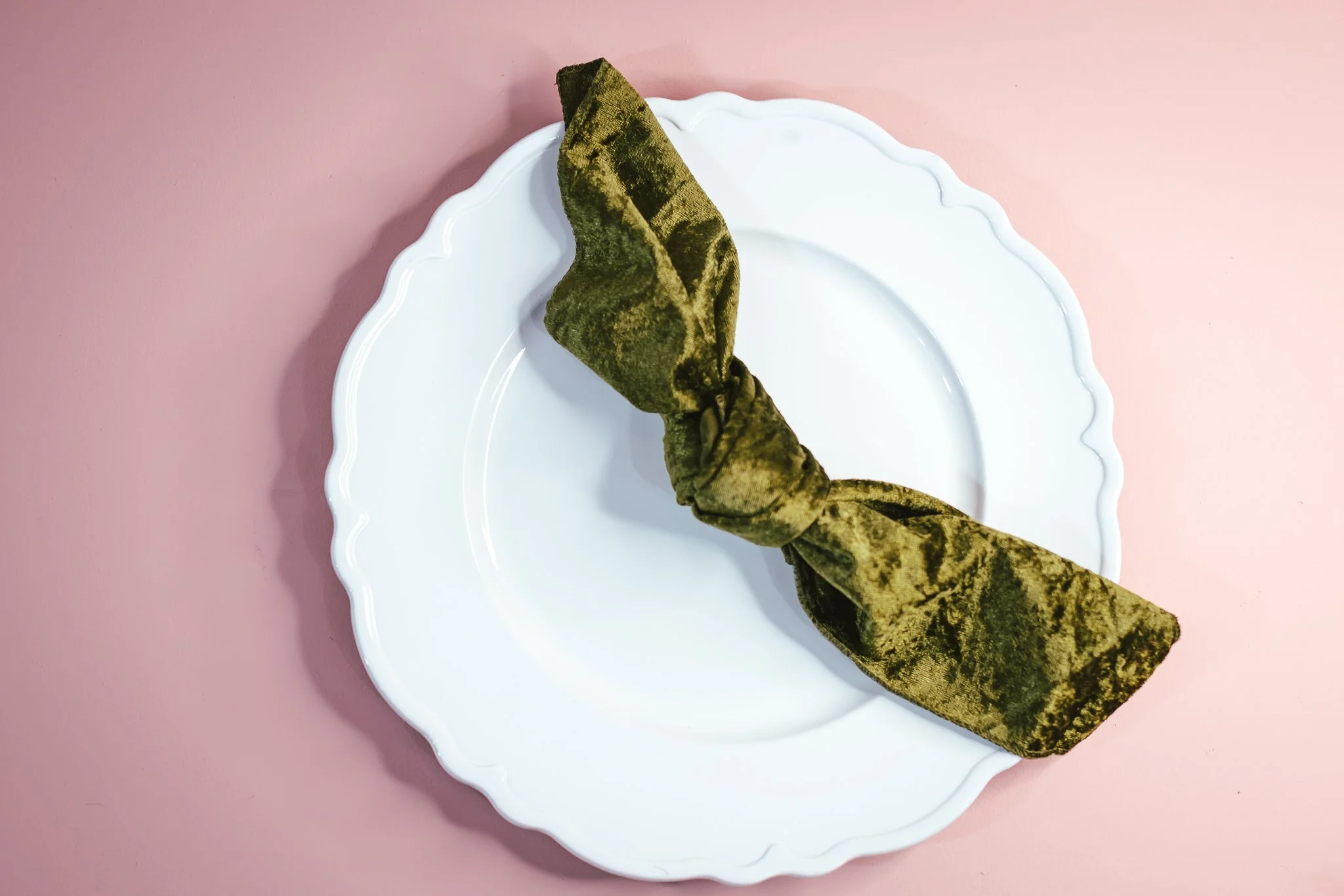 A white decorative plate on a pink surface and green velvet napkin.