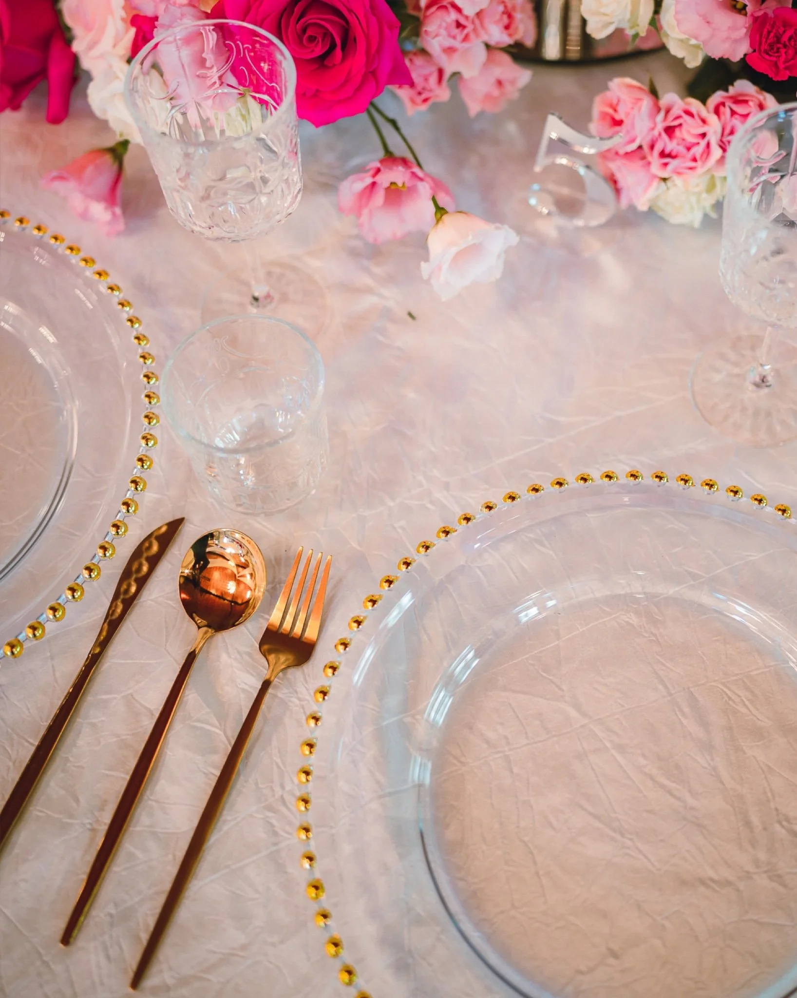 A table setting with pink and white flowers, glassware, gold utensils, and decorative elements.