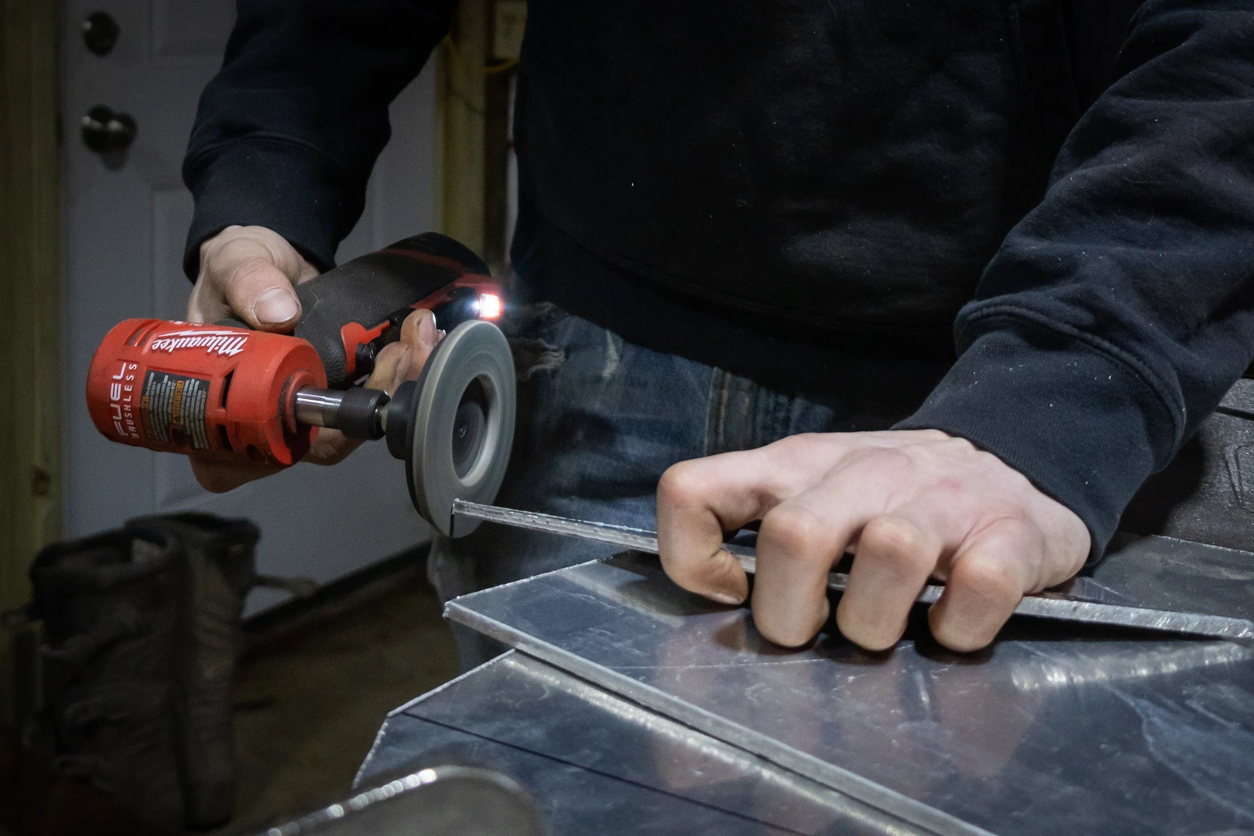 Person using a handheld angle grinder to cut or grind a metal piece in a workshop.