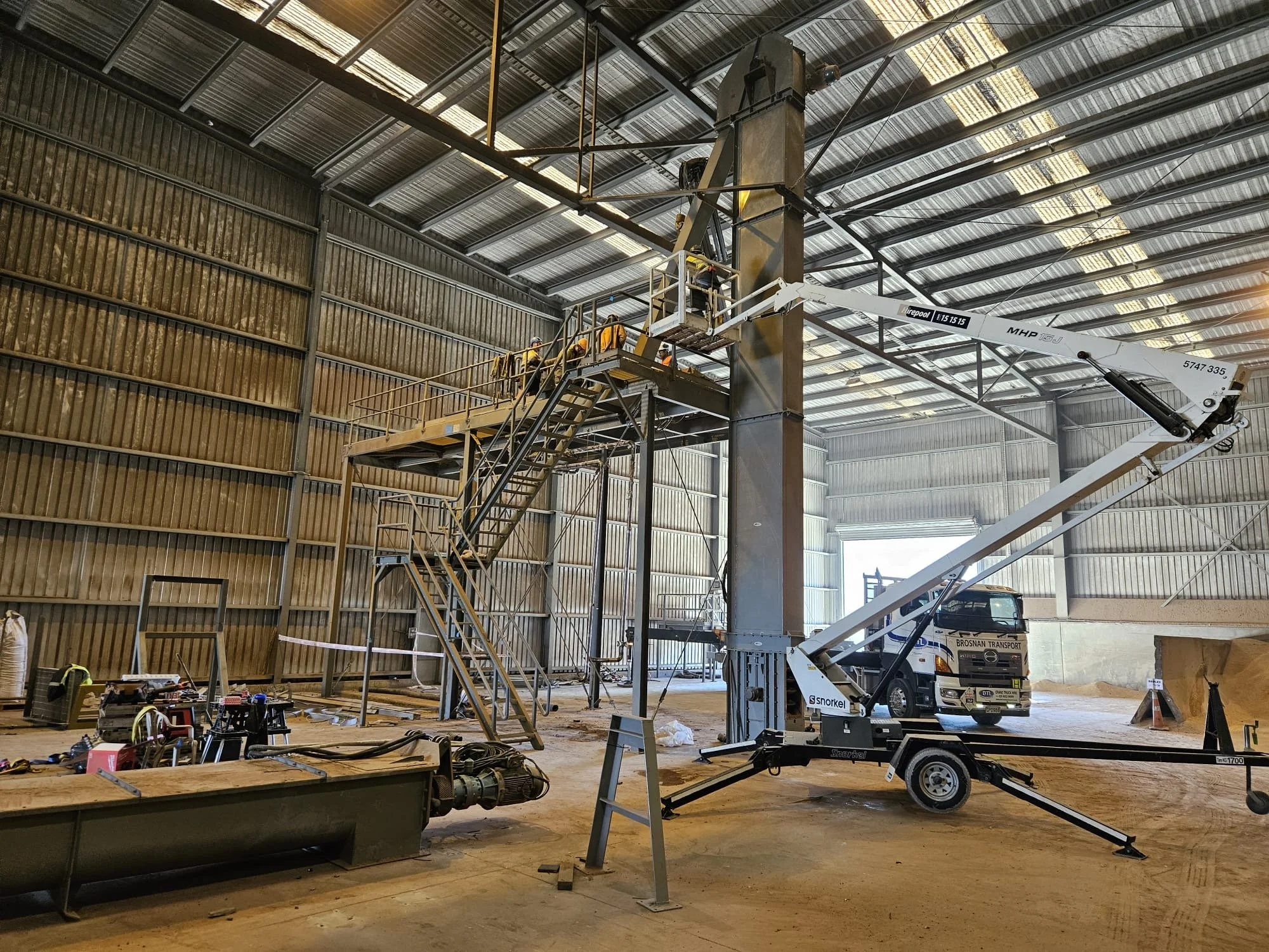 Superior Engineering Group - Construction workers in safety gear using a lift inside a large industrial building under construction, with tools and machinery scattered on the floor.