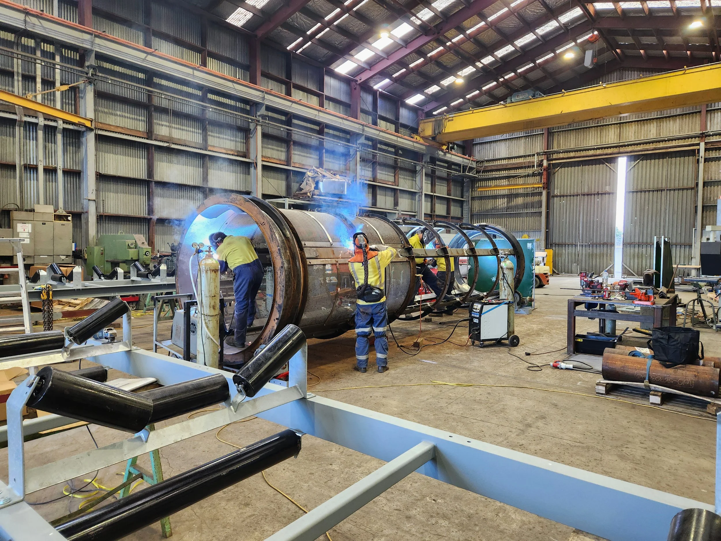 Superior Engineering Group - Workers welding large cylindrical metal pipes inside an industrial warehouse.