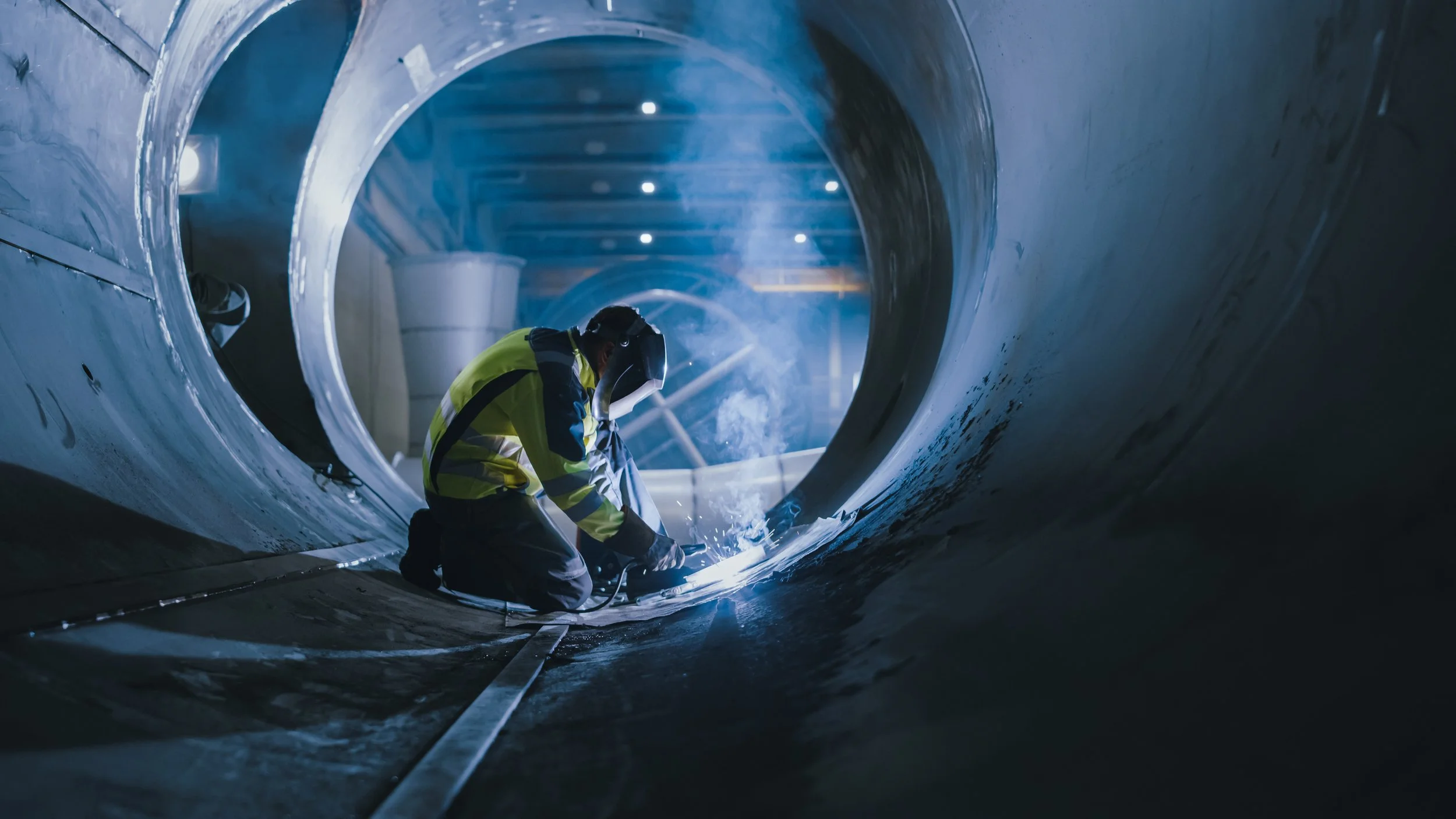 Superior Engineering Group - A worker welding inside a large, cylindrical metal structure in an industrial setting, with sparks and smoke visible.