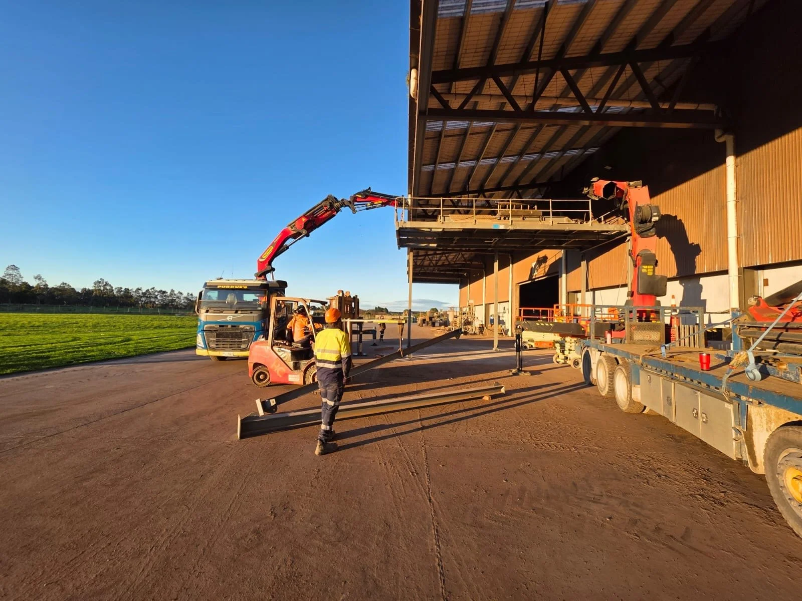 Superior Engineering Group - Construction workers in safety gear working near a building, with heavy machinery and equipment, under a clear sky.
