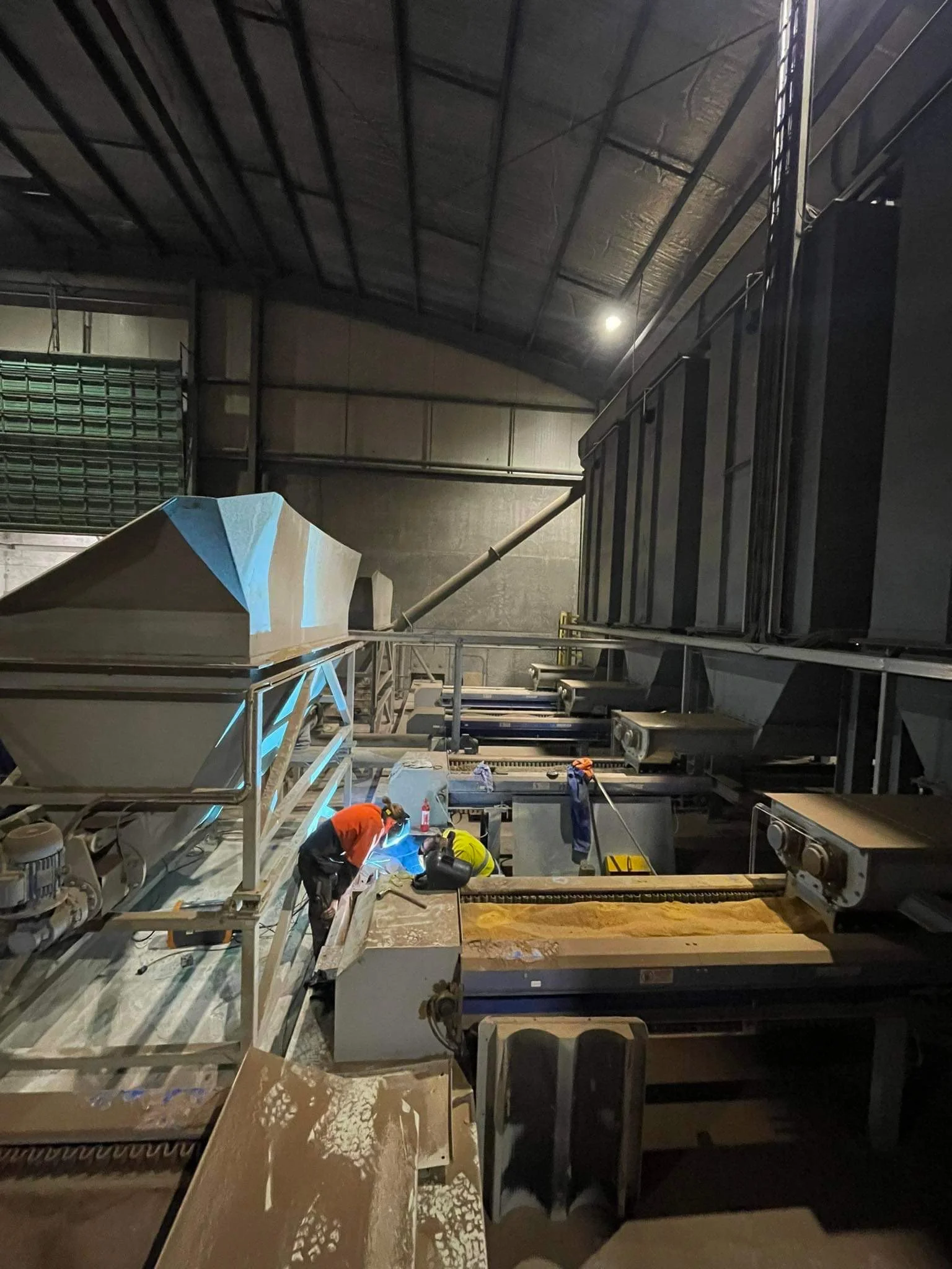 Superior Engineering Group - Two workers are welding inside a large industrial or warehouse space with a high, curved ceiling. Various equipment and machinery are visible around them.