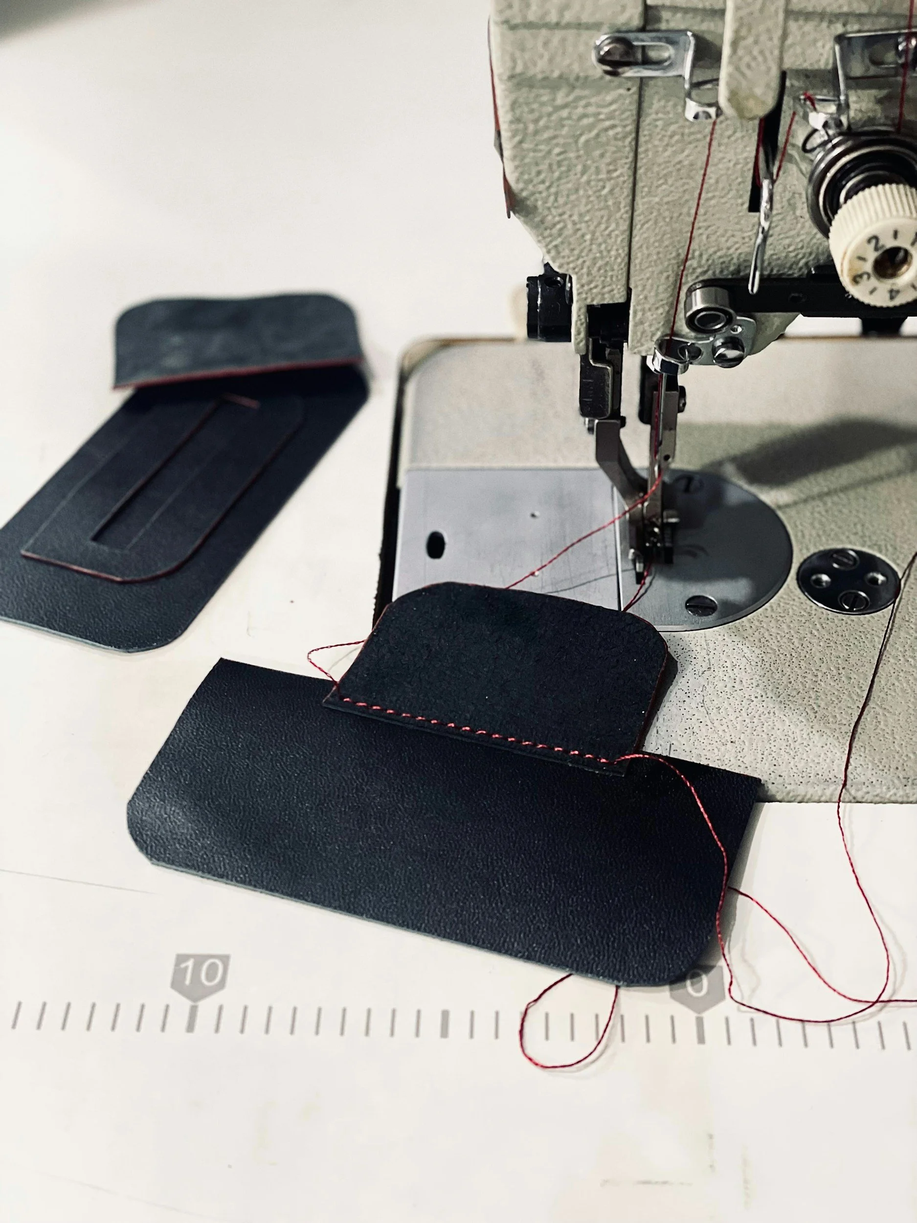 Close-up of sewing machine stitching black fabric, with sewing accessories and a ruler in the background.