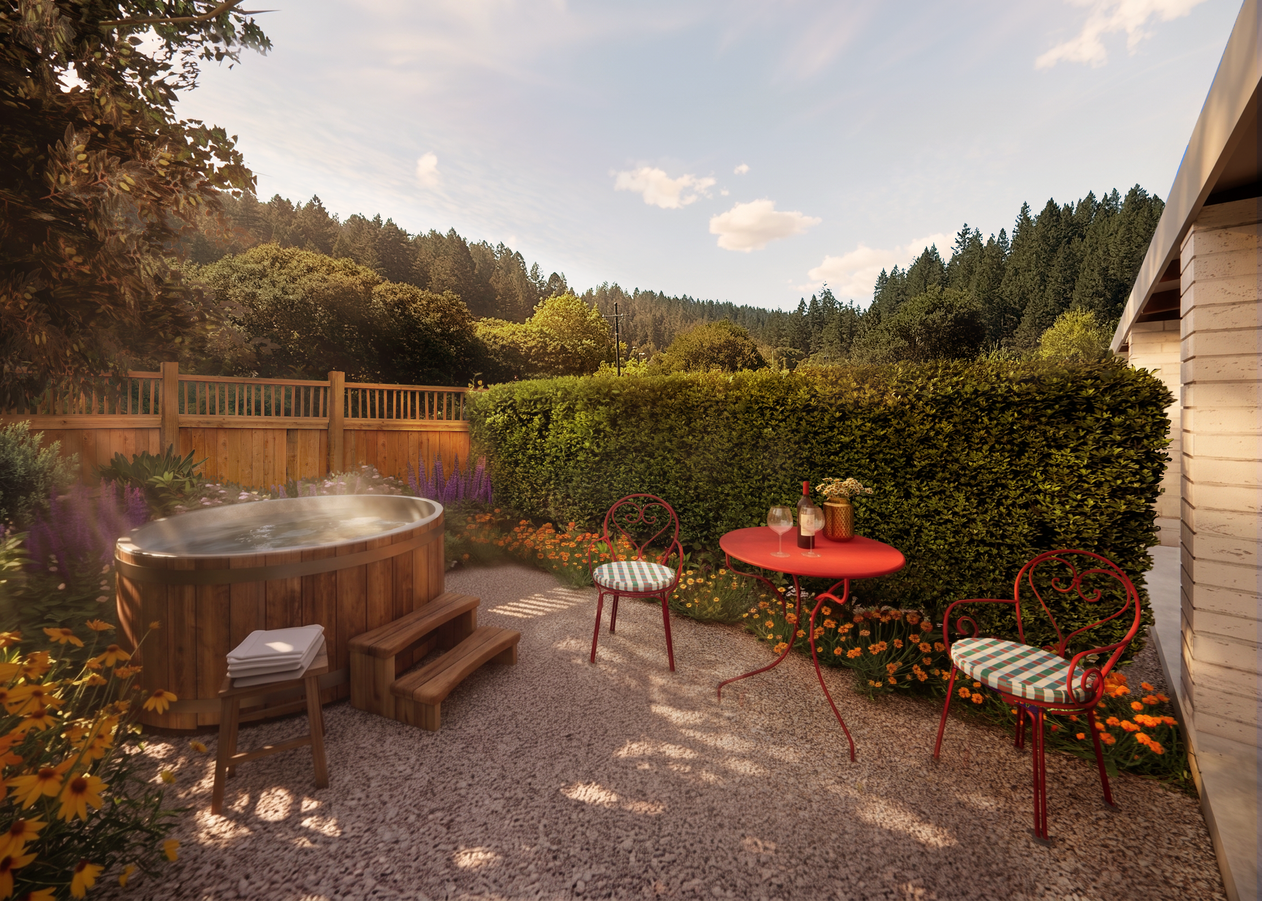 A backyard patio with a hot tub, red metal chairs with checkered cushions, a small round red table with a wine bottle, glasses, and a candle, surrounded by colorful flowers and green bushes, with a view of a wooded hillside and blue sky with clouds.