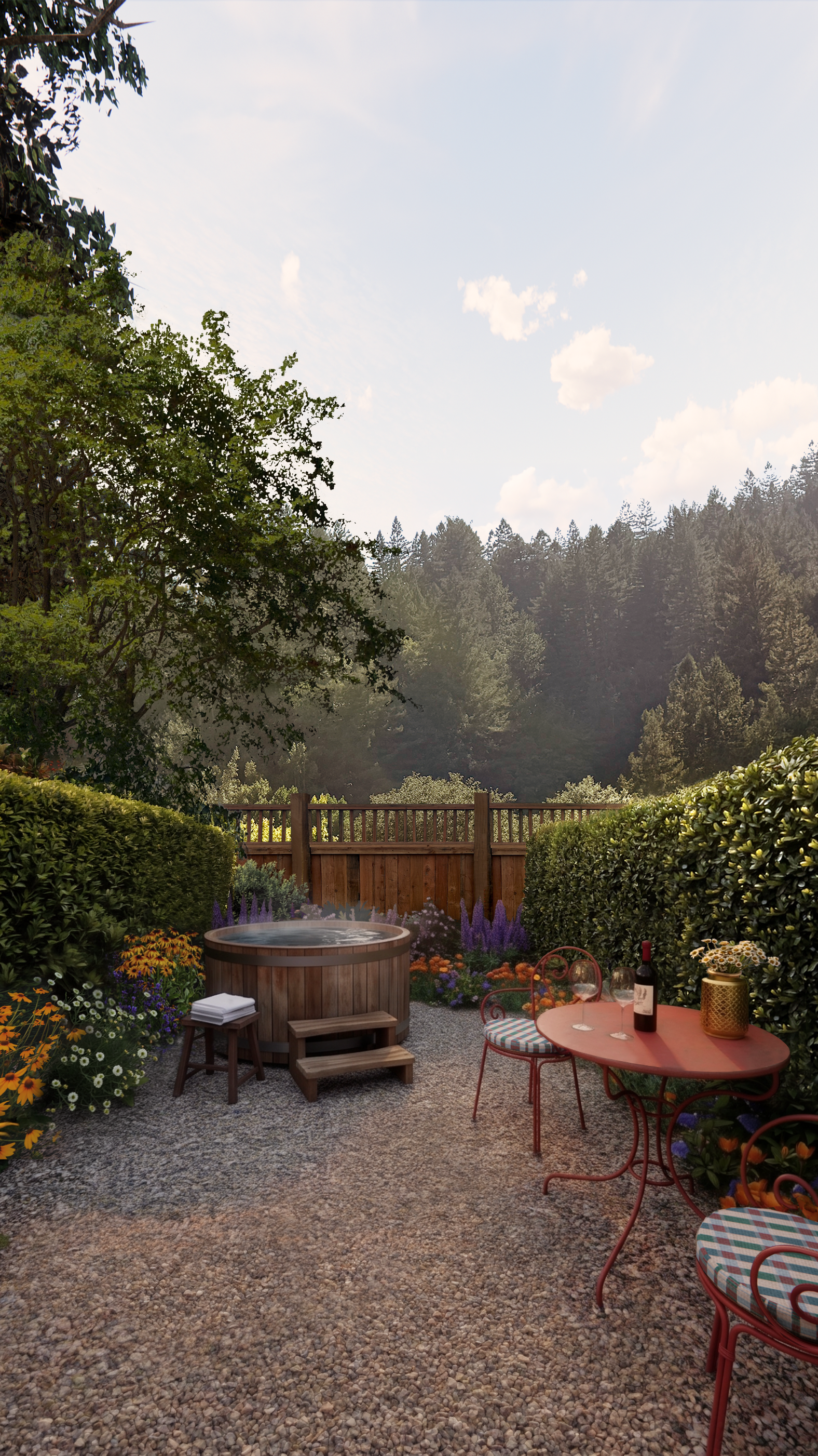 An outdoor patio with a gravel floor, featuring a round table with two chairs, a bottle of wine, glasses, and a lantern. There is a hot tub and a garden with colorful flowers, surrounded by bushes and trees, with a wooden fence and forest in the background, under a partly cloudy blue sky.