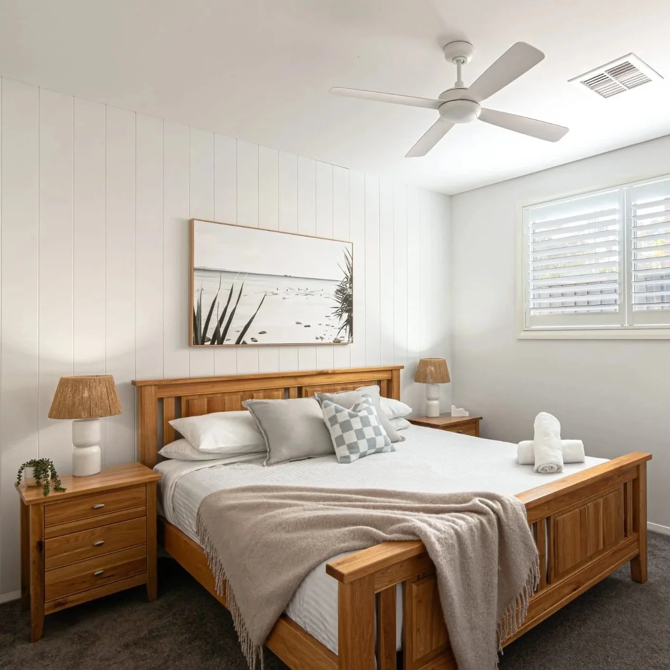 Guest bedroom with timber bed frame, neutral bedding, and coastal art styled by Terra Styling — Kiama