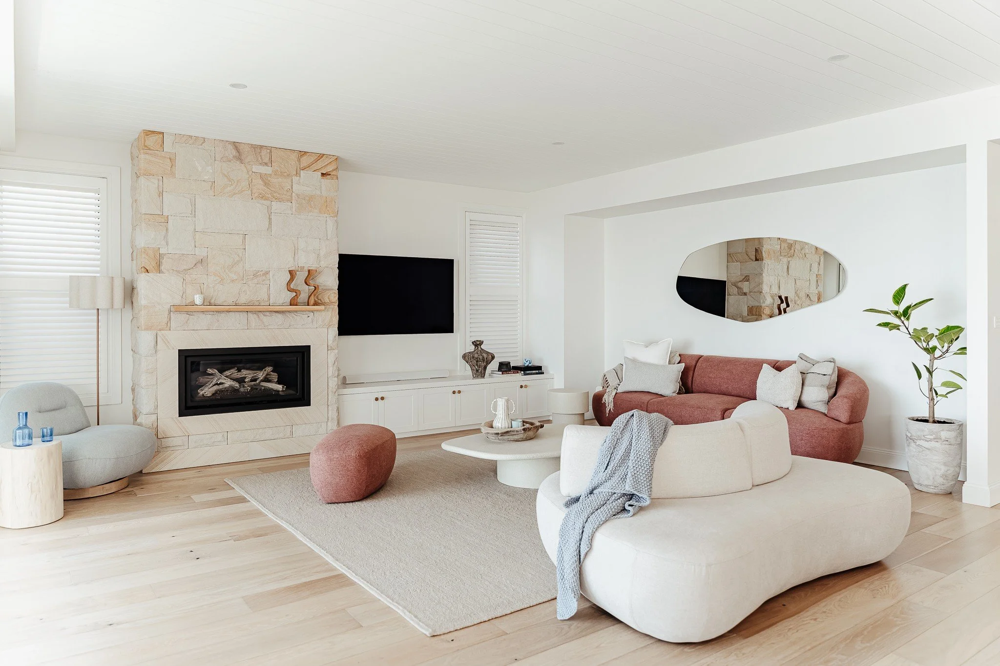 Coastal living room with stone fireplace, curved sofa, and natural textures styled by Terra Styling — Kiama Downs