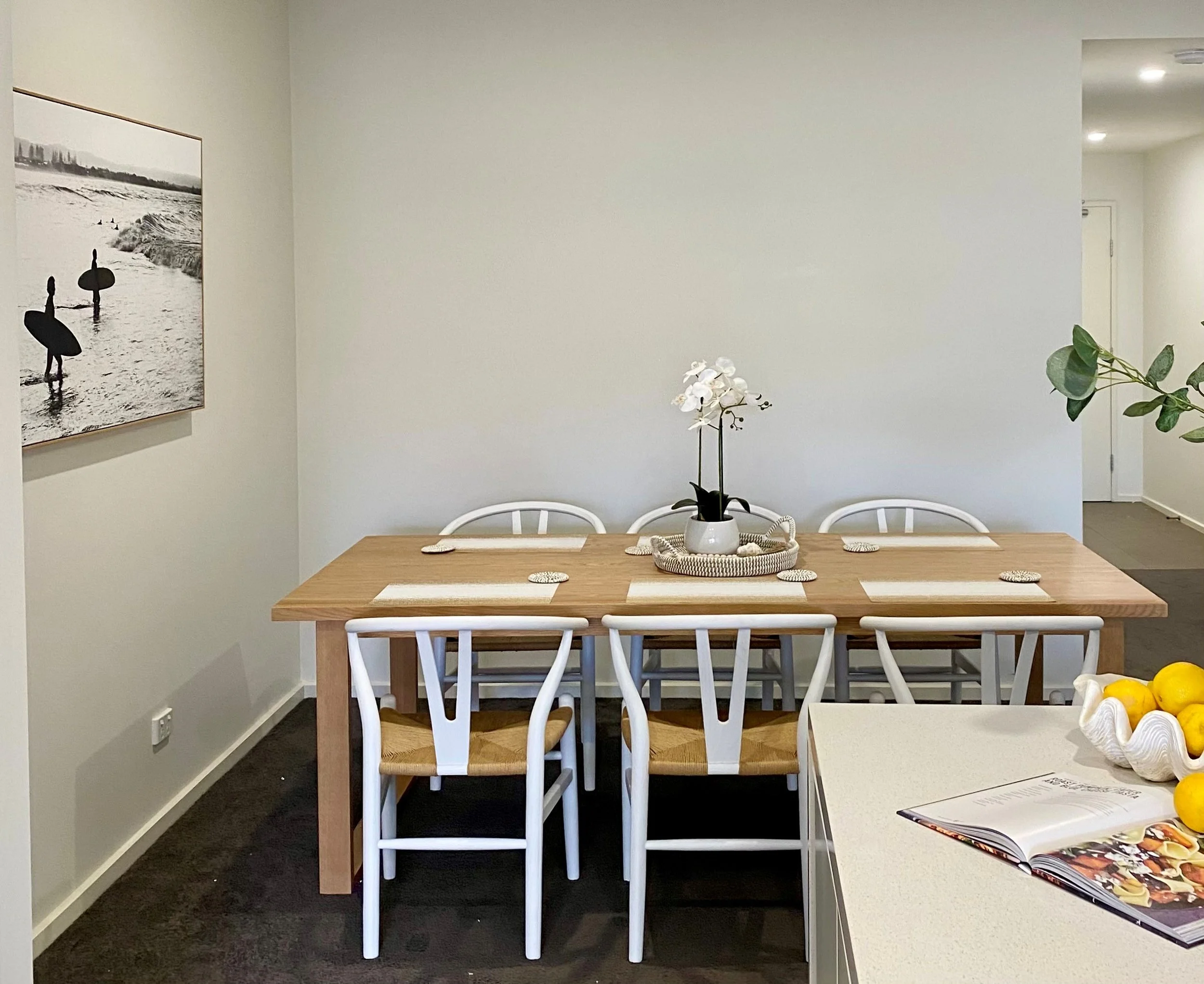 Dining room with timber table, white chairs, and coastal artwork styled by Terra Styling — holiday rental Kiama
