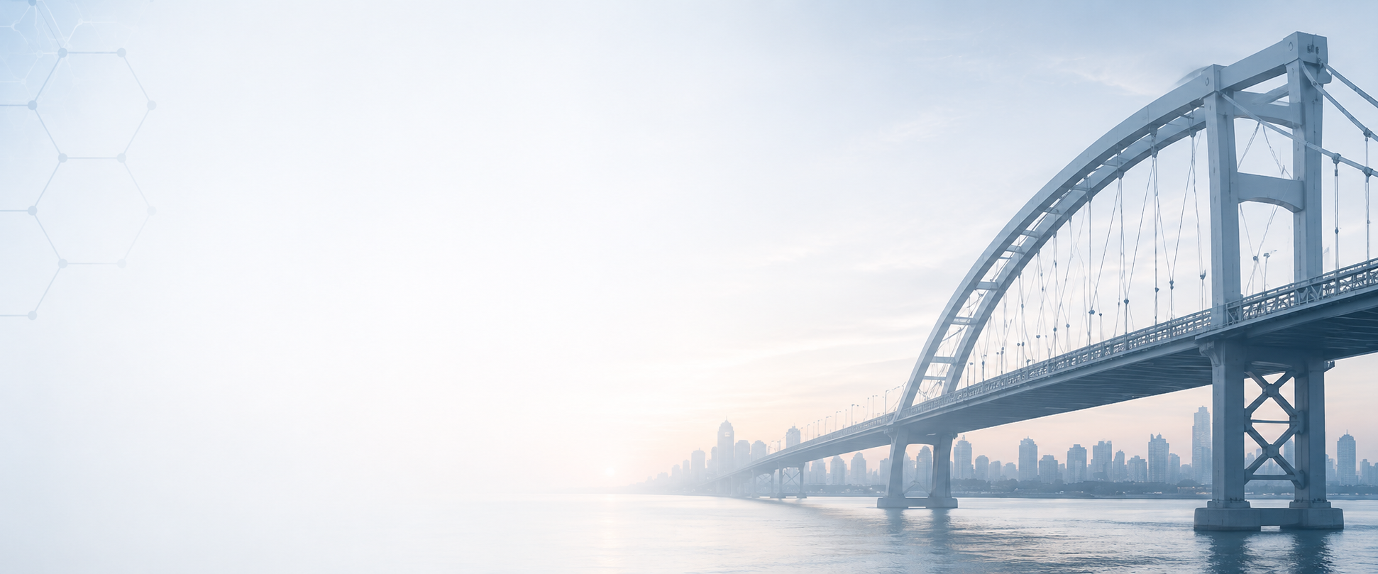 A large suspension bridge extending over water with a city skyline in the background under a partly cloudy sky.