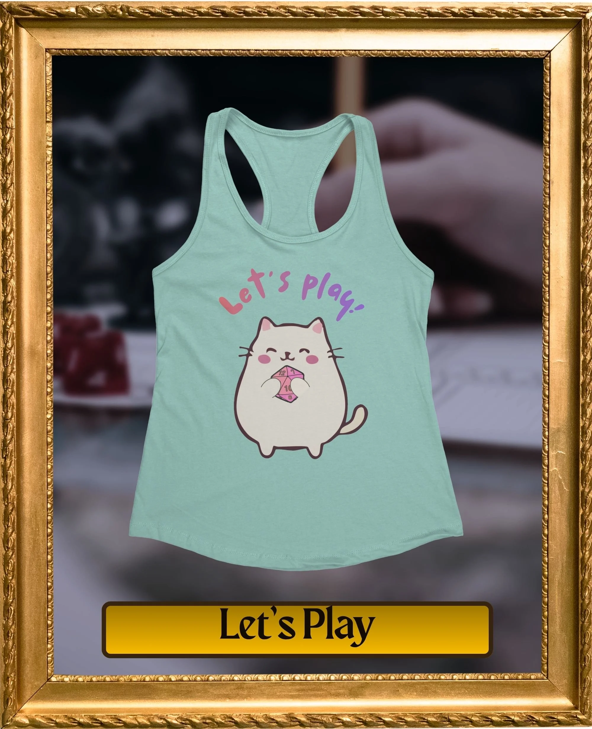 A mint green tank top with a cartoon cat holding a pink die, with the text "Let's Play!" above the cat, framed with a gold ornate border.