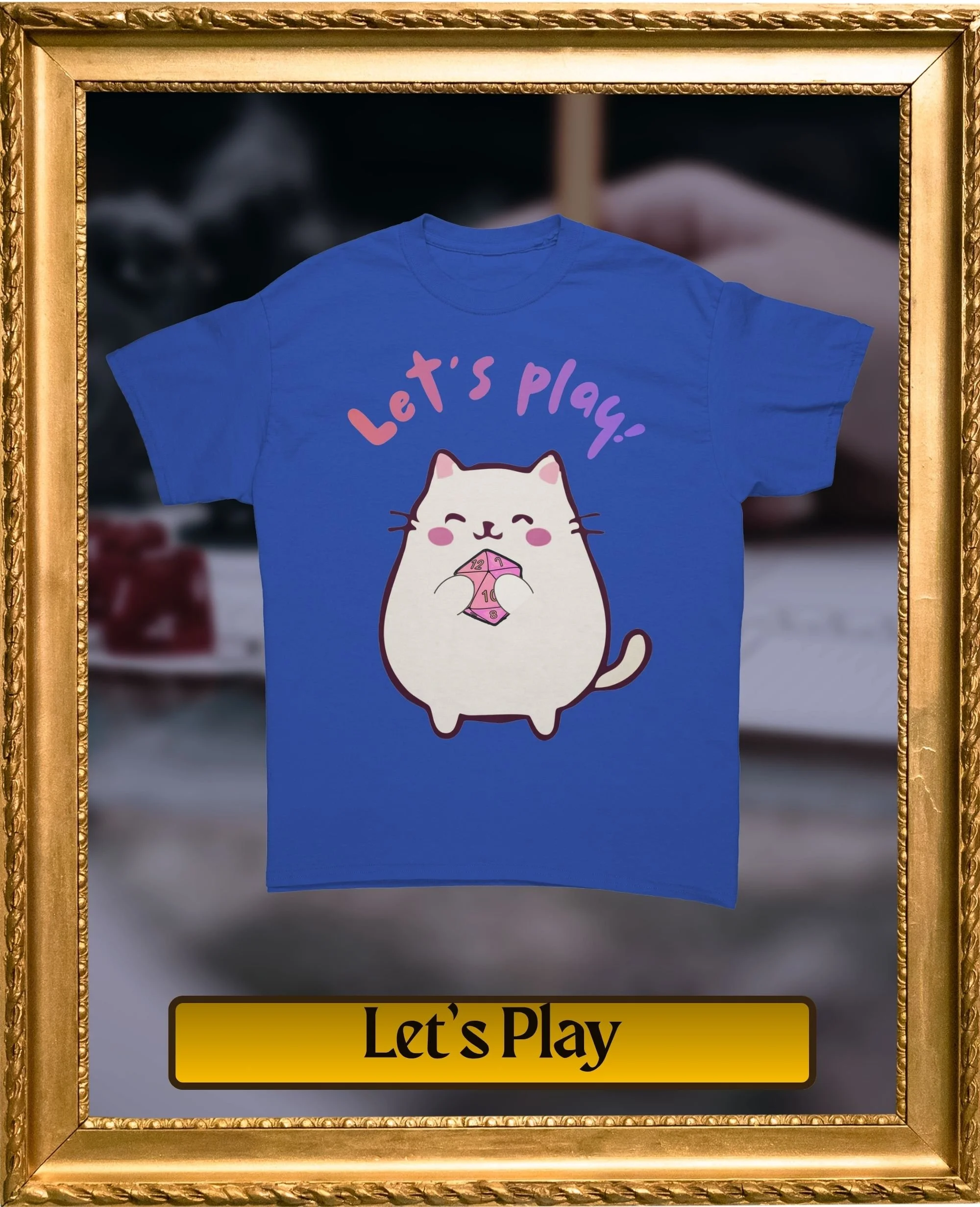 Blue T-shirt with a cartoon cat holding a die and the words "Let's play!" in pink and purple text.