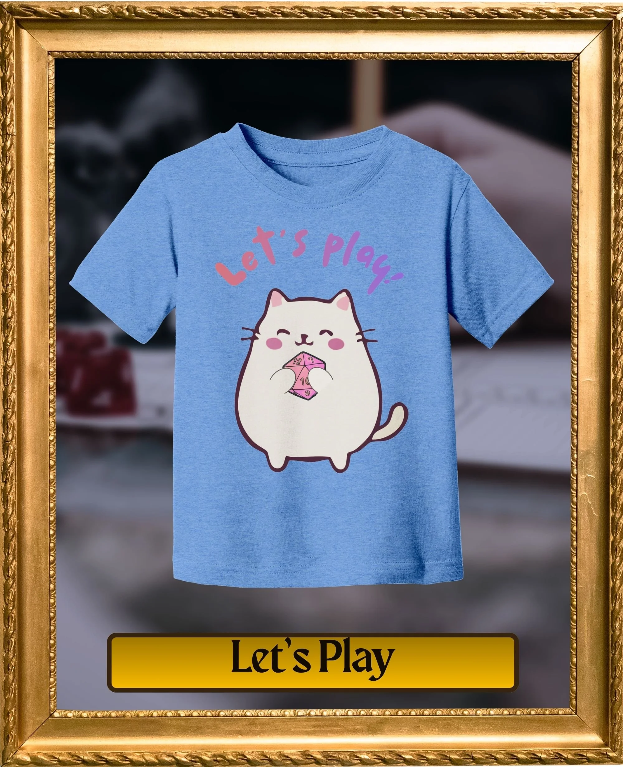 Blue T-shirt with cartoon cat holding a pink dice and the text 'Let's Play' in pink and purple letters.