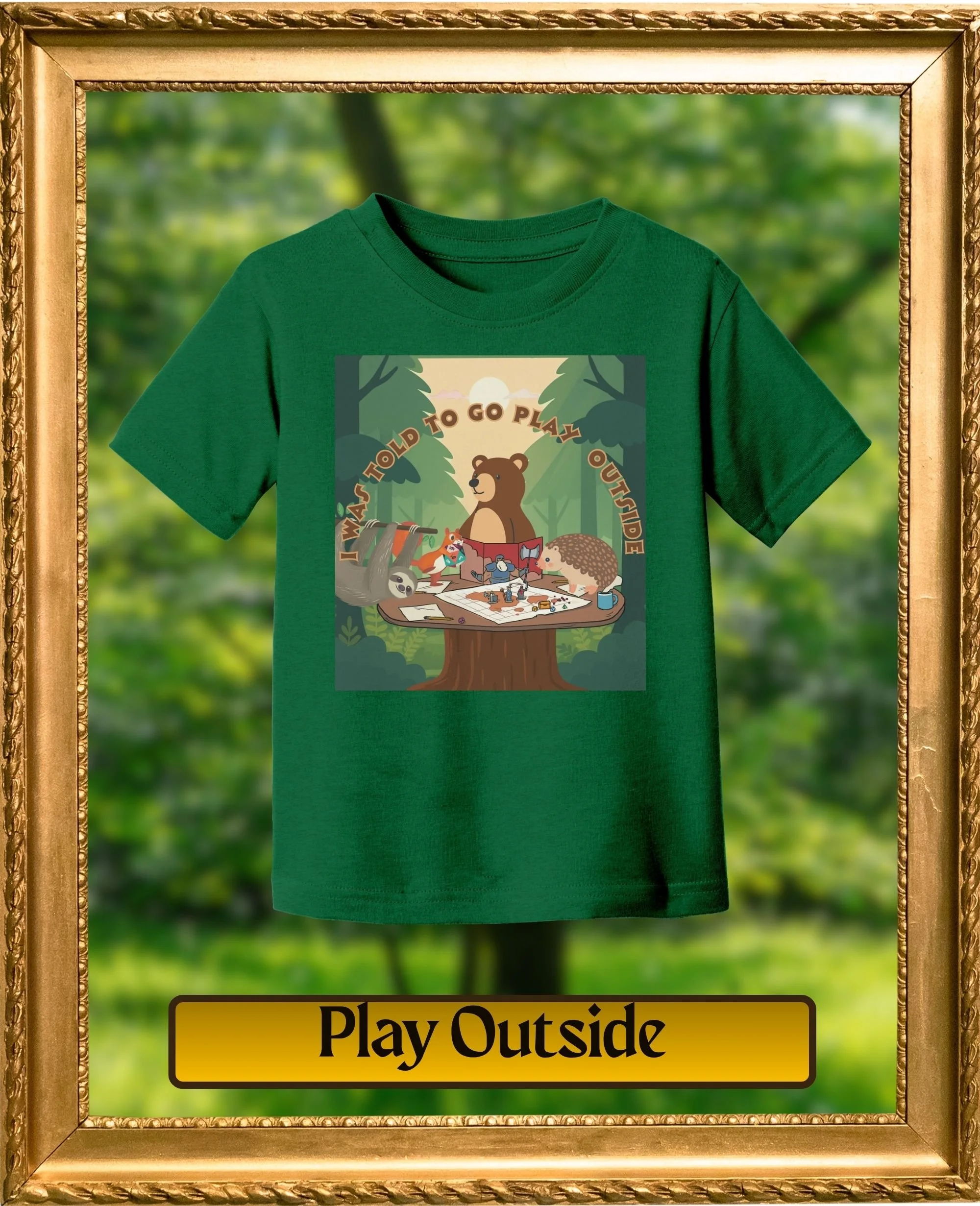 Green T-shirt with a cartoon illustration of a bear and other animals around a table, with the text "I was told to go play outside." The T-shirt is displayed inside a gold ornate frame with a blurred outdoor background.
