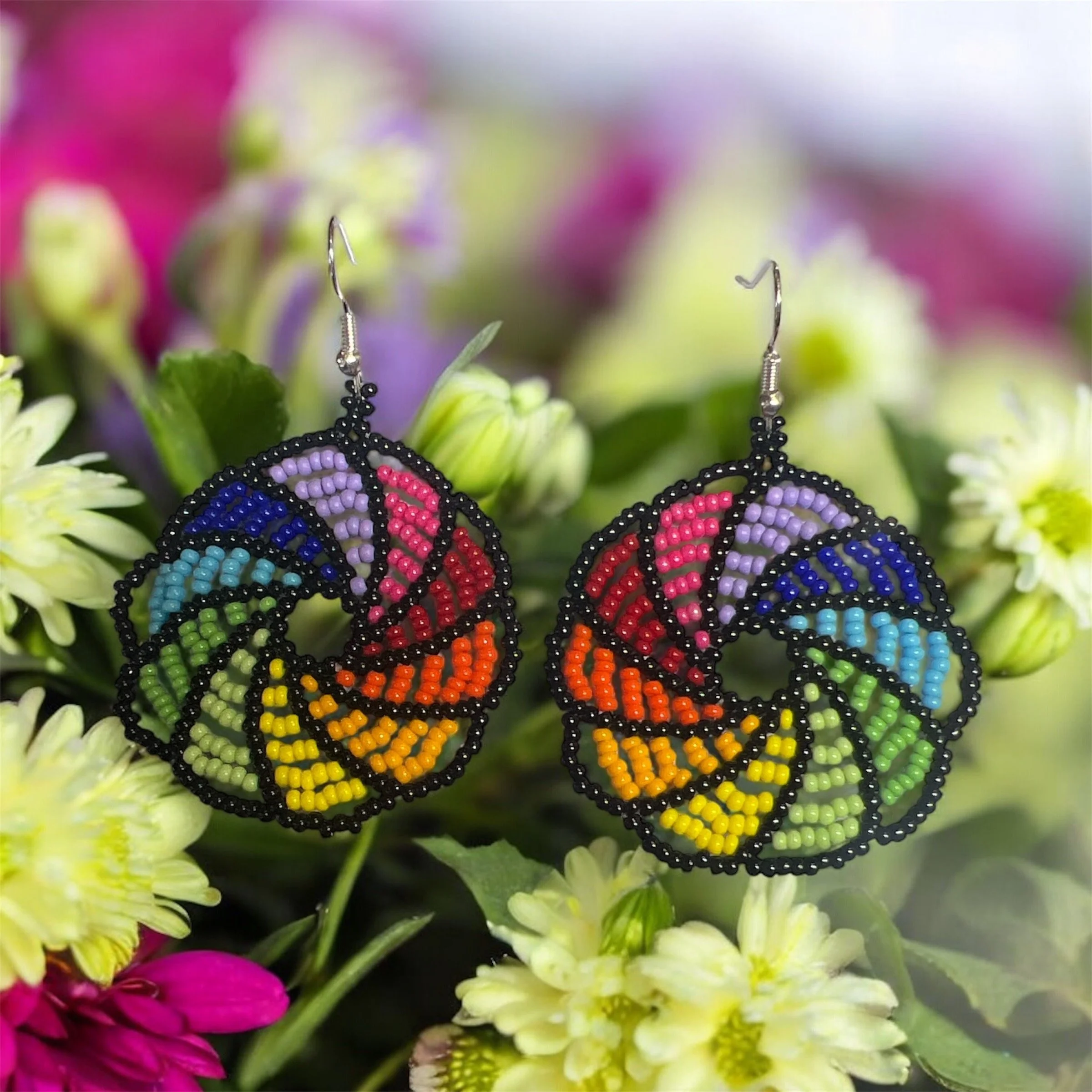 Colorful butterfly earrings with pink, purple, blue, green, yellow, orange, red, and black beads hanging among yellow and pink flowers.