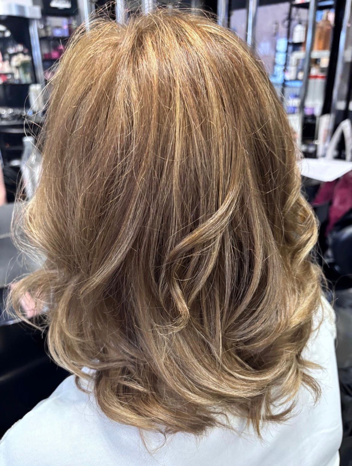 A woman with styled, shoulder-length, curly blonde hair in a salon setting.