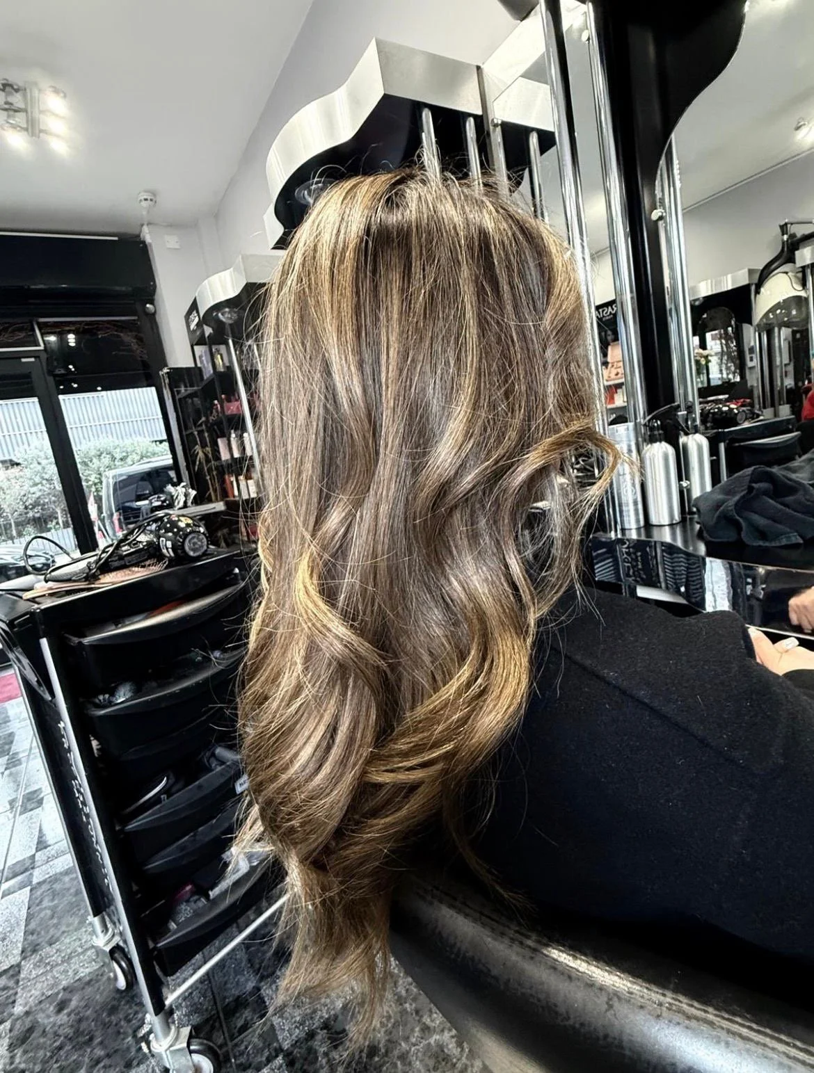 A woman with voluminous, wavy blonde hair sitting in a salon chair inside a modern salon.