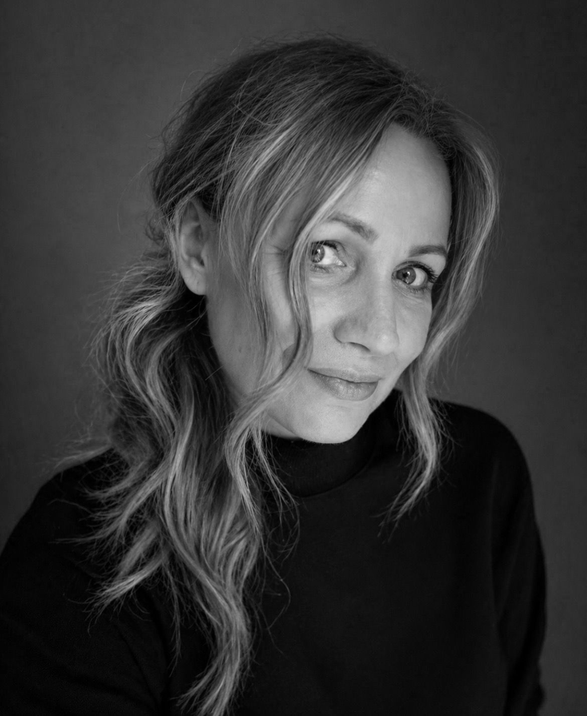 Black and white portrait of a woman with wavy hair and a gentle expression, wearing a dark top.