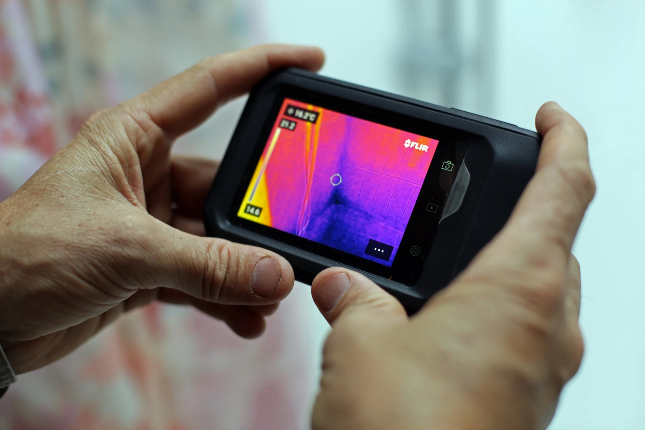Person holding a thermal imaging camera displaying a colorful thermal image