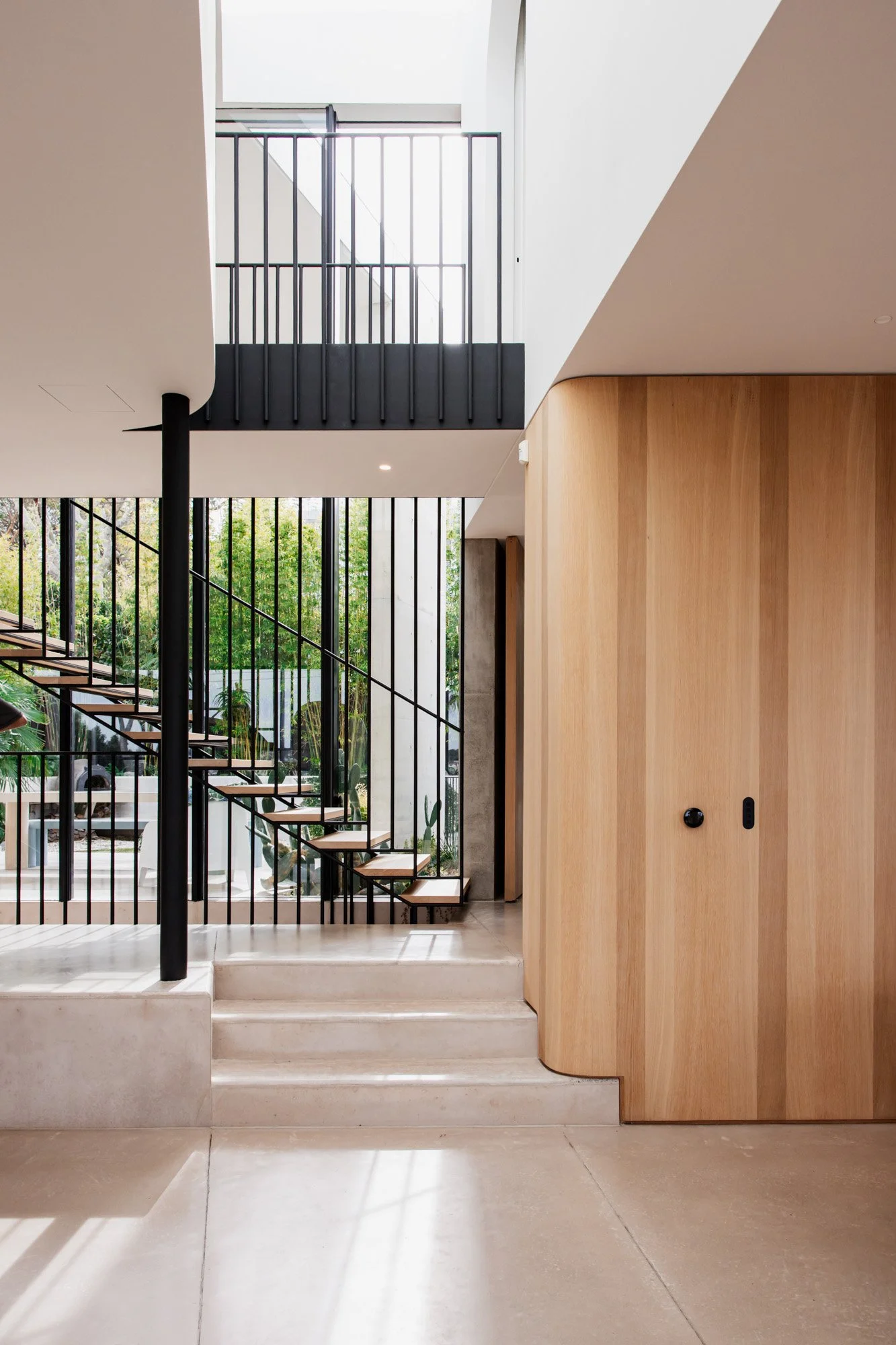 Interior view of a modern home with stairs, black metal railings, a large window, and wooden wall panels.