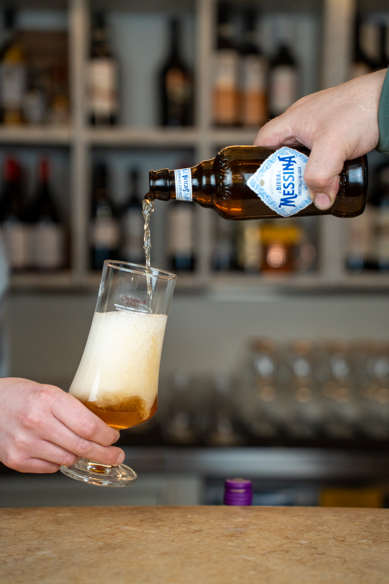 Una mano versa una birra da una bottiglia in un bicchiere, con una schiuma cremosa sopra.