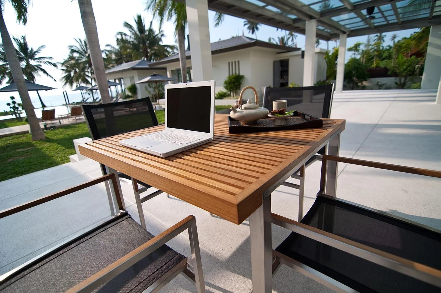 Outdoor dining table with a laptop and tea set at a tropical resort.