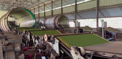 Industrial machine processing large cylindrical rolls and conveyor belts in a factory setting.