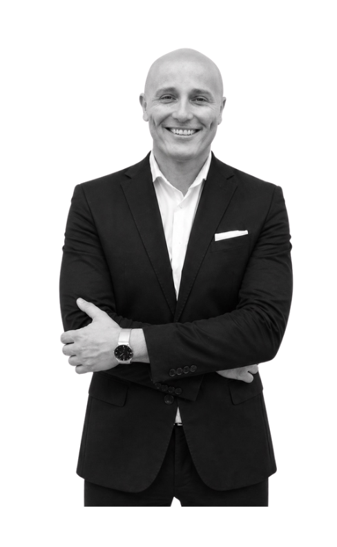 Black and white photo of a smiling man in a suit with arms crossed, standing against a plain background.