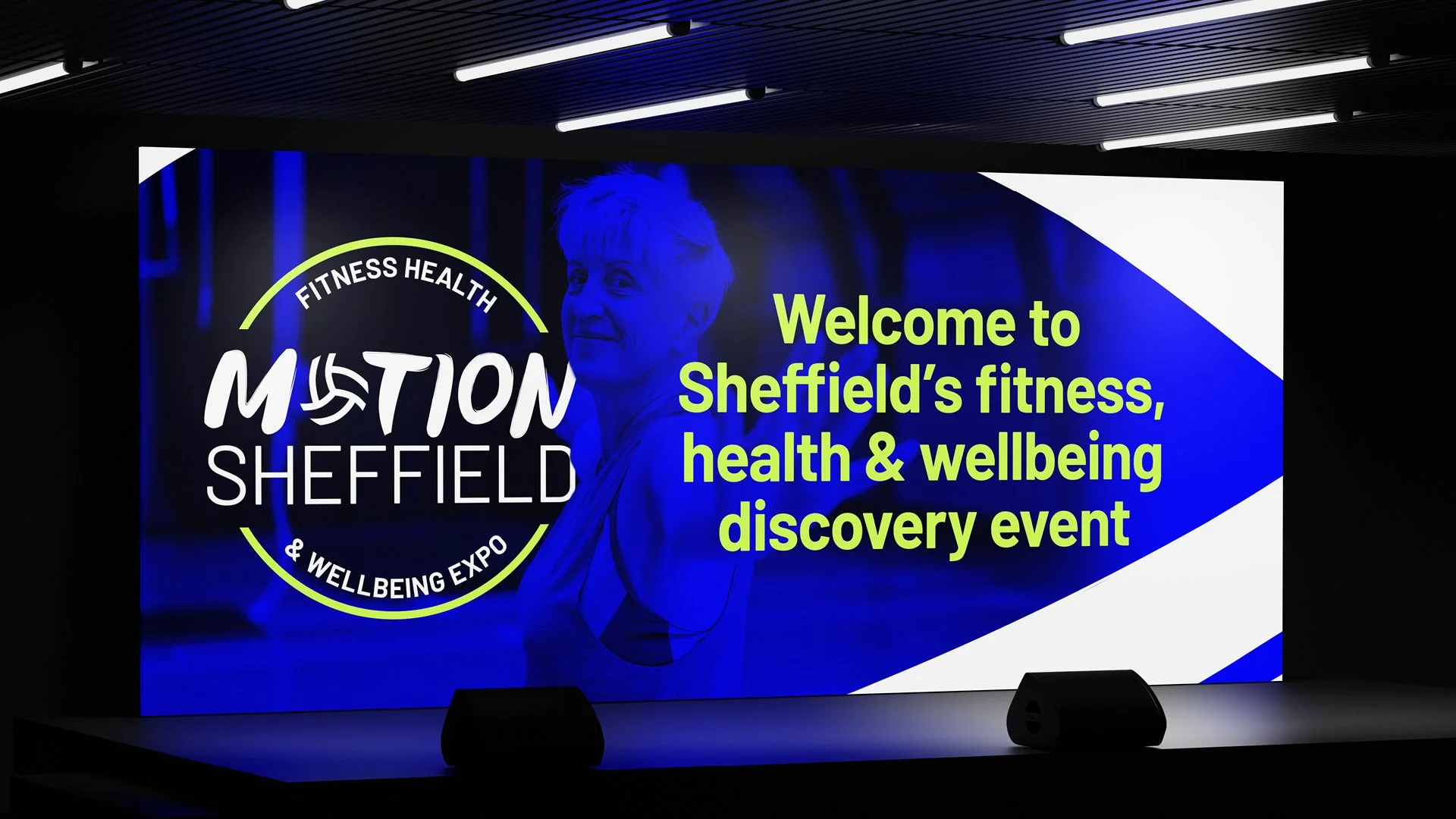 Large digital screen displaying a welcome message for Sheffield's fitness, health, and wellbeing discovery event, featuring a woman in the background and bright green and white text.