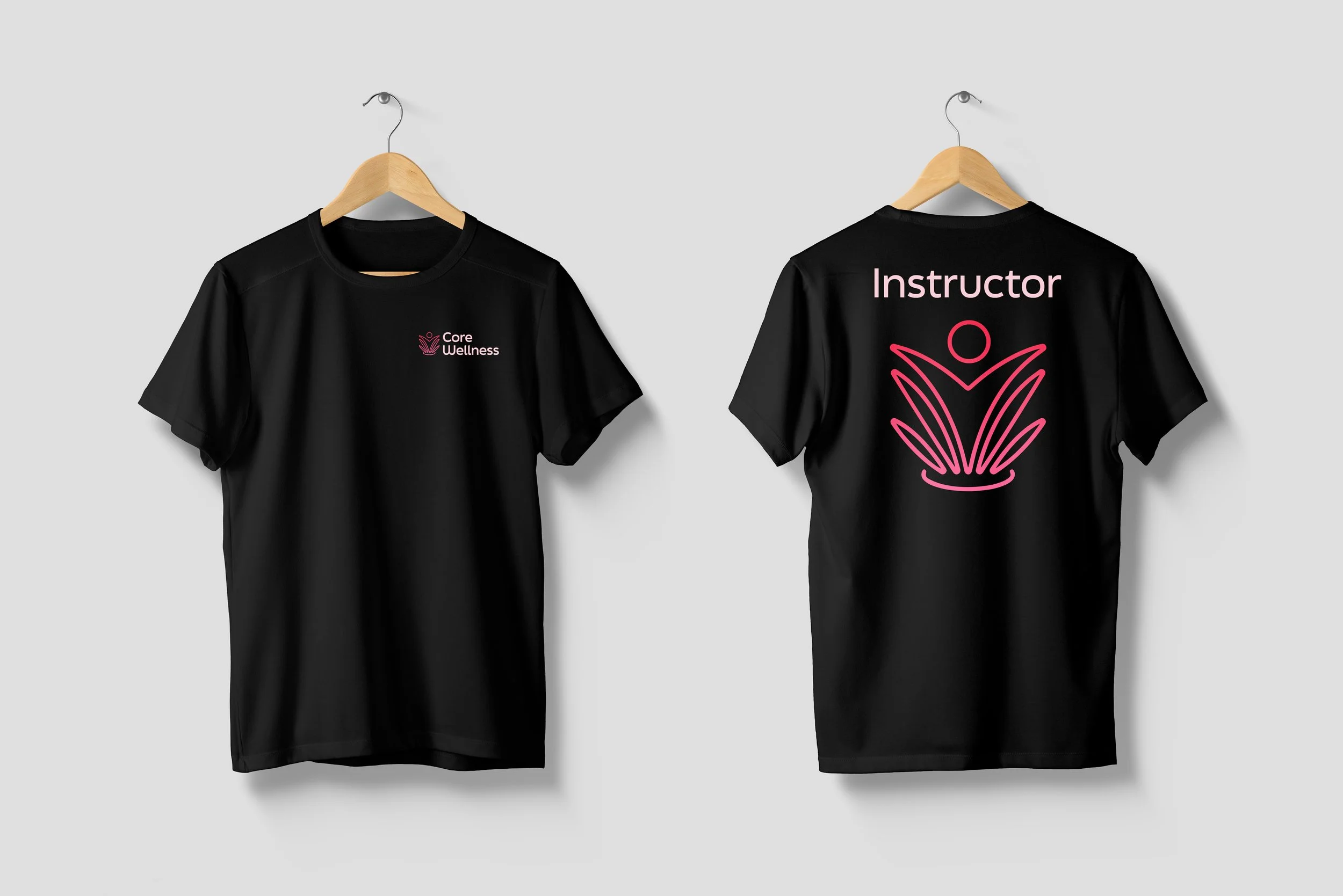Black T-shirts hanging on wooden hangers against a light gray background. The front of the T-shirt has a pink logo for 'Core Wellness,' and the back has the word 'Instructor' and a line drawing of a person doing yoga.