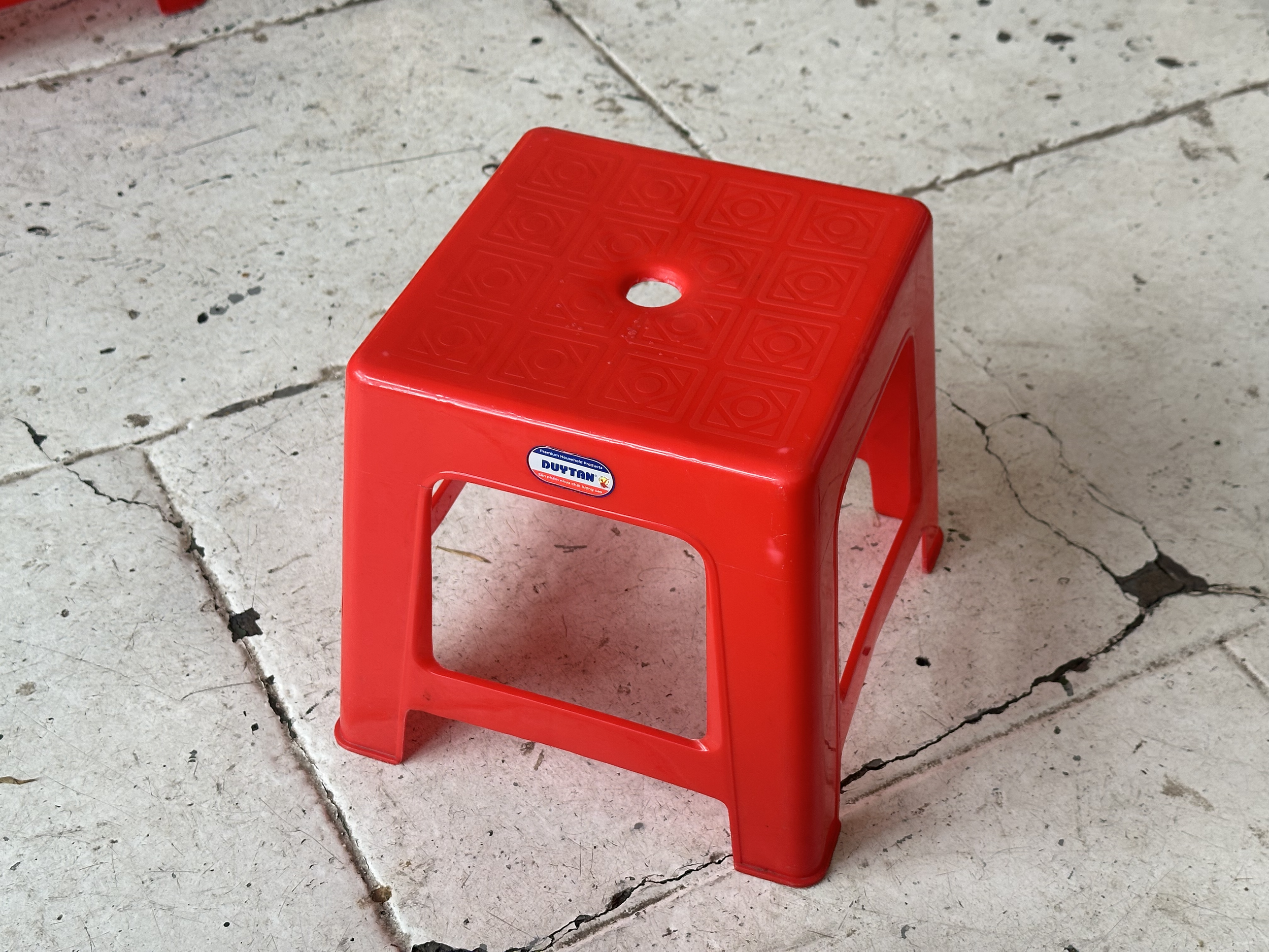 Red plastic step stool on cracked concrete ground.