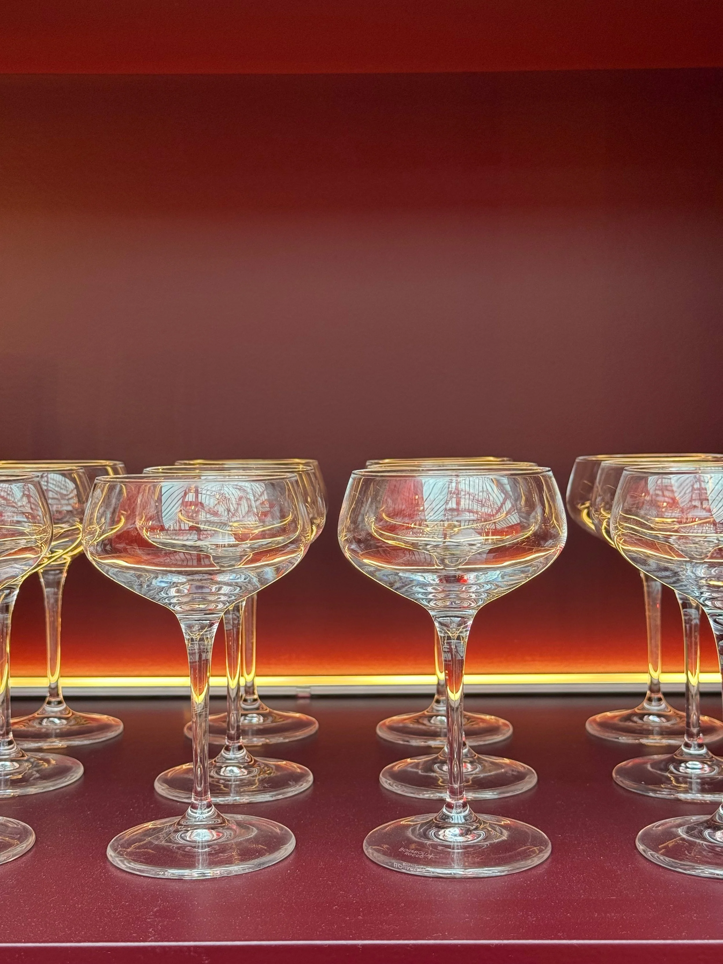 Multiple empty wine glasses arranged in rows on a red surface with a dark red background.