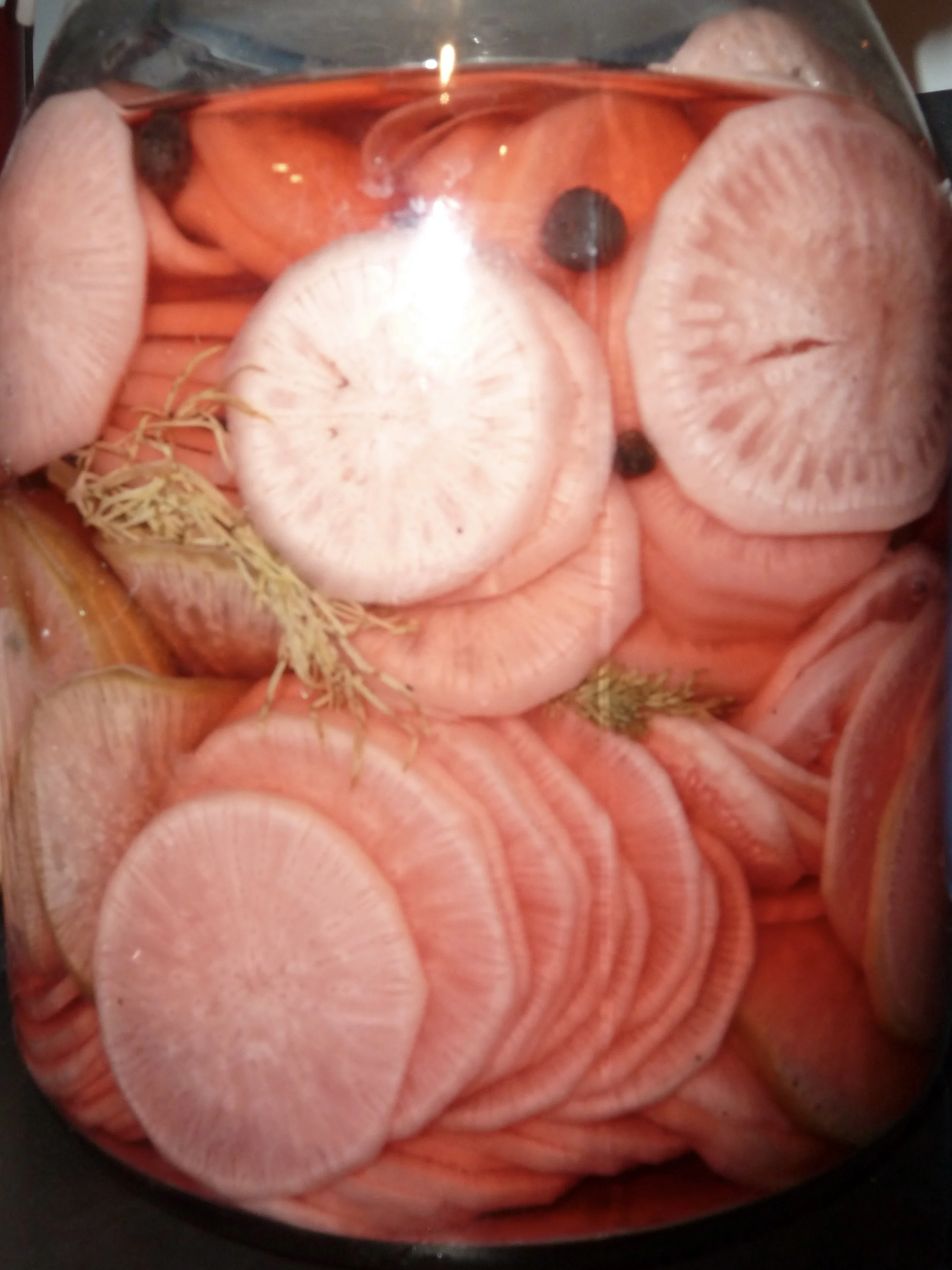 Canned sliced turnip with black peppercorns and herbs on top.