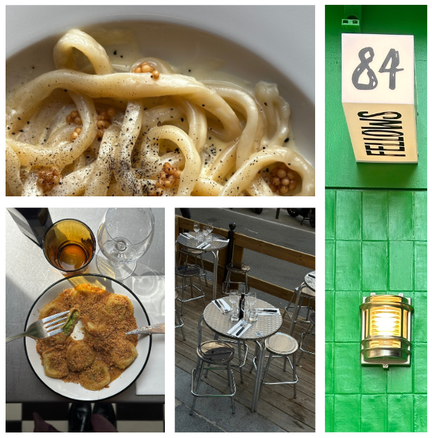 Close-up of a bowl of fettuccine pasta with cream sauce, black pepper, and small bits of herbs; a plate, a glass of wine, and a glass of water on a table; outdoor seating with a small round table and four chairs on a wooden deck; a green wall with a yellow lantern and a sign