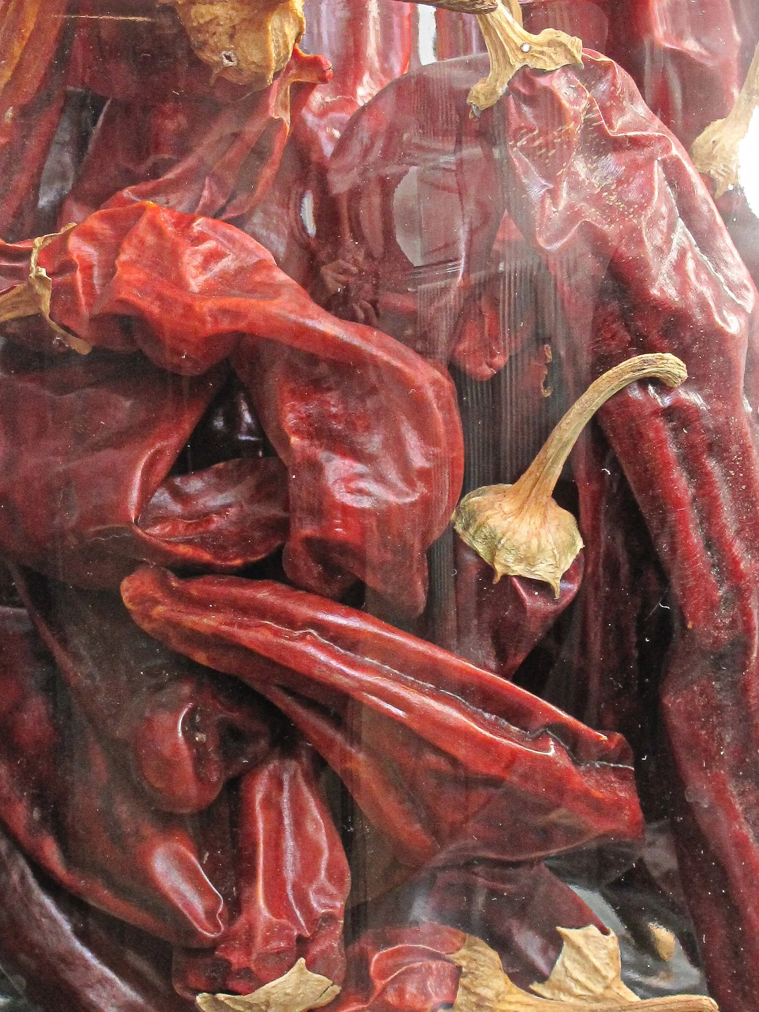 Dried red chili peppers with a few brownish dried leaves inside a transparent container.