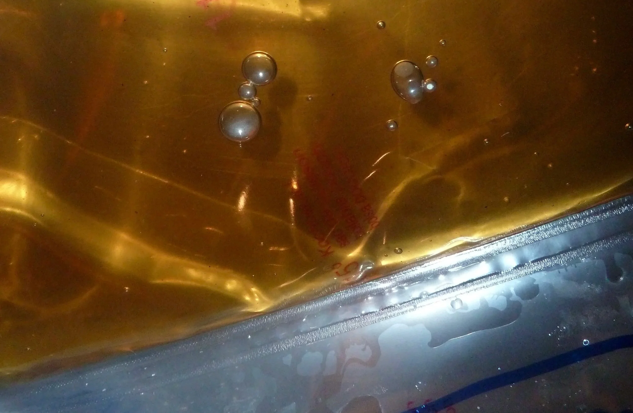 Close-up of bubbles forming in a golden liquid surface inside a metallic container.