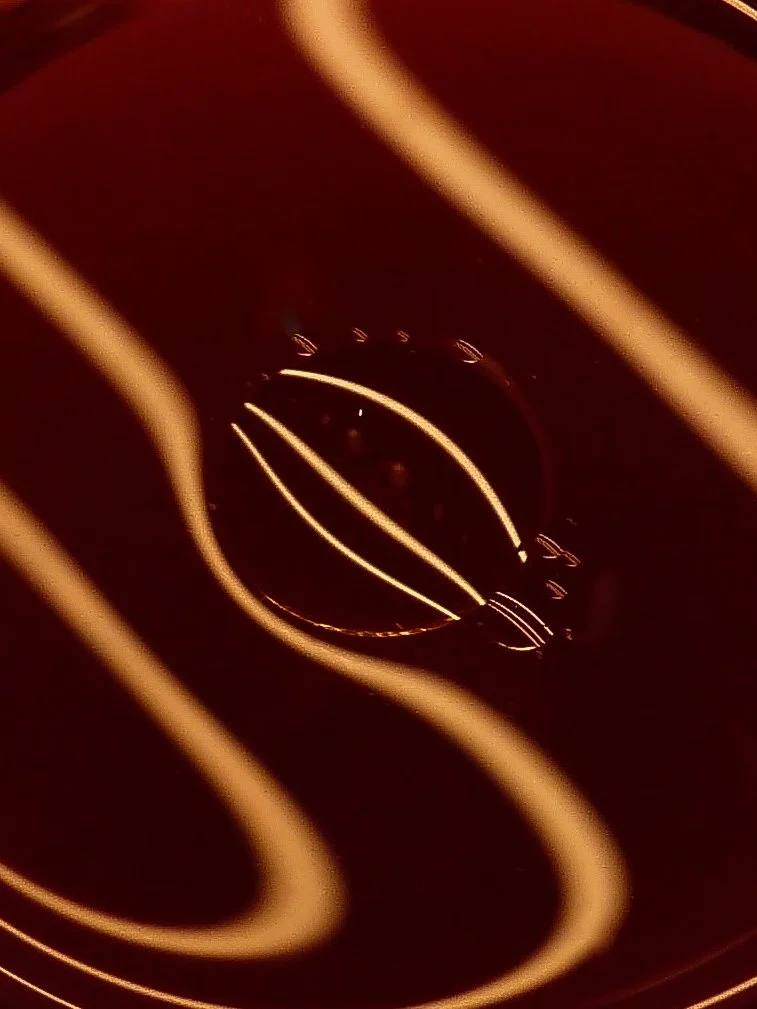 Close-up of a dark-colored object with glowing light lines, possibly a glass or bottle viewed from above with reflections and abstract lighting.
