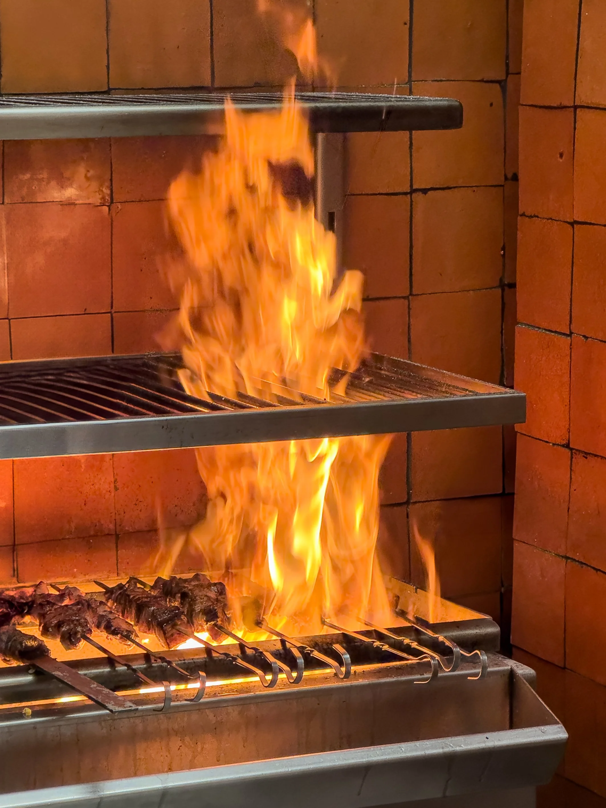 Flames and fire over a grill with skewered meat at a restaurant or kitchen.