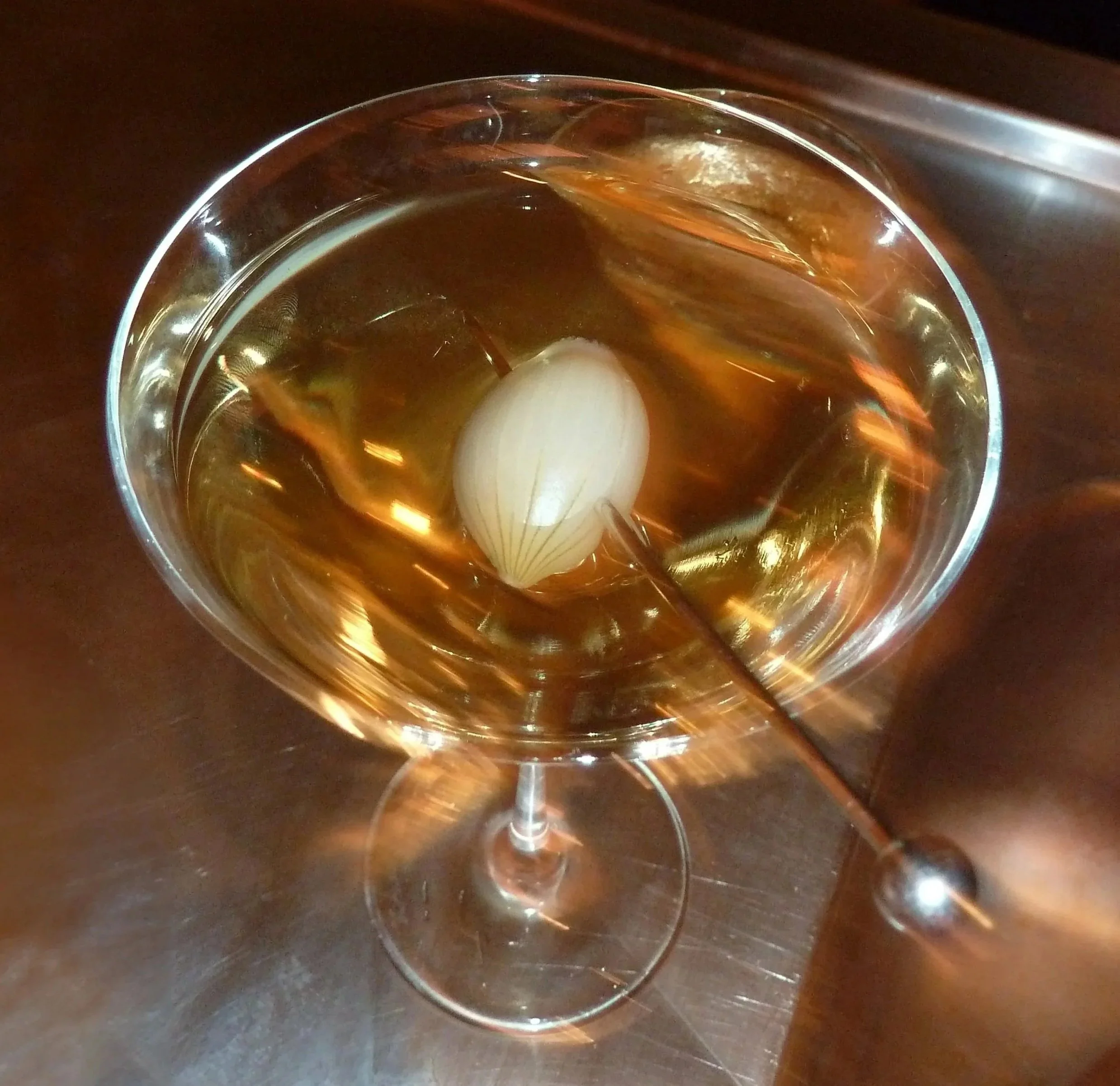 Top view of a clear glass filled with a dark amber-colored liquid and pickled spring onion inside, placed on a dark surface.