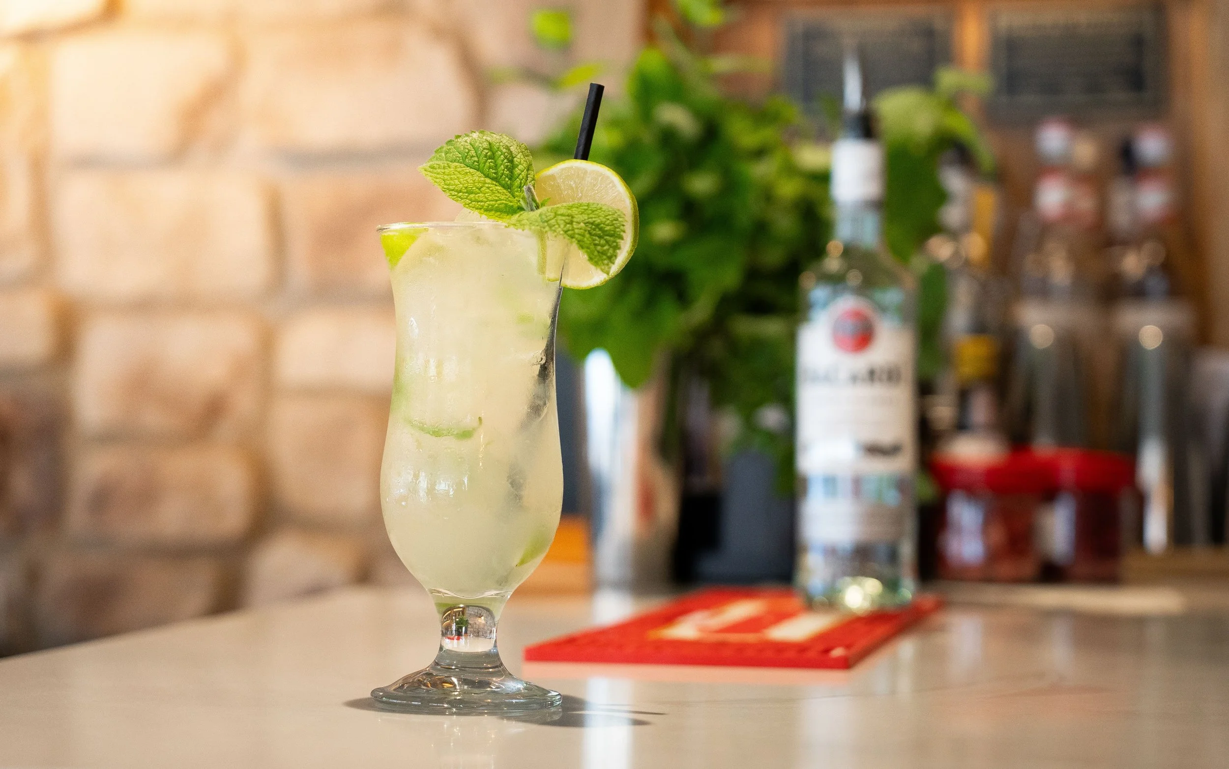 A tall glass of lemonade garnished with a lemon slice and mint leaves, with ice inside, sitting on a bar counter.